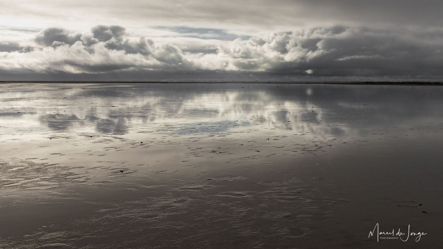 Dramatic panoramic view of dark storm clouds rolling over a vast lake with moody reflections on the water's surface.