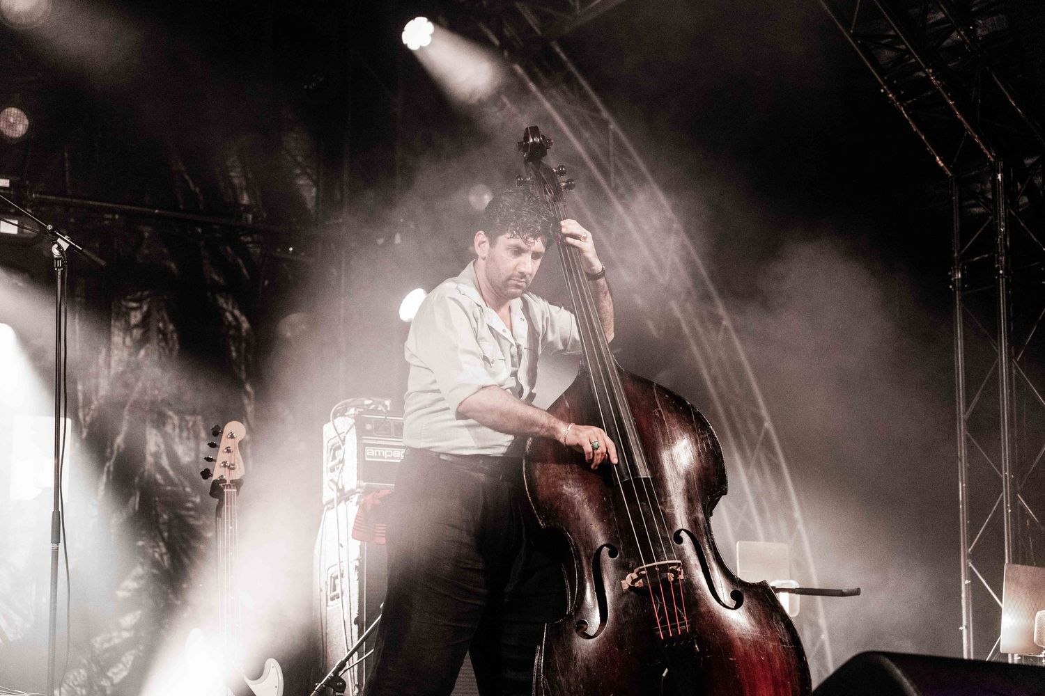 Musician playing double bass on stage with dramatic lighting and fog at an outdoor concert.