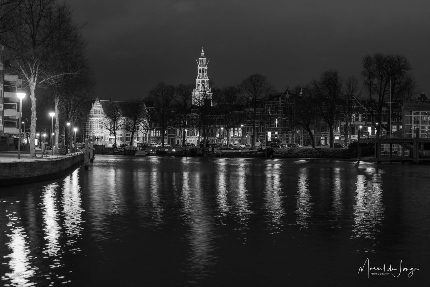 Black and white panoramic cityscape of Amsterdam canals and historic buildings illuminated at night with reflections on water.