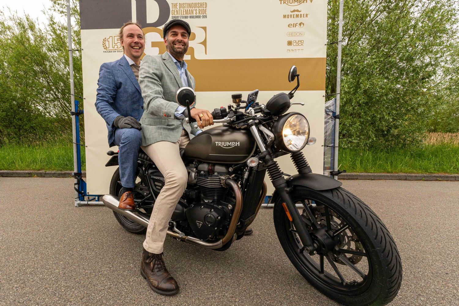 Two men posing with a Triumph motorcycle outdoors at an award event.