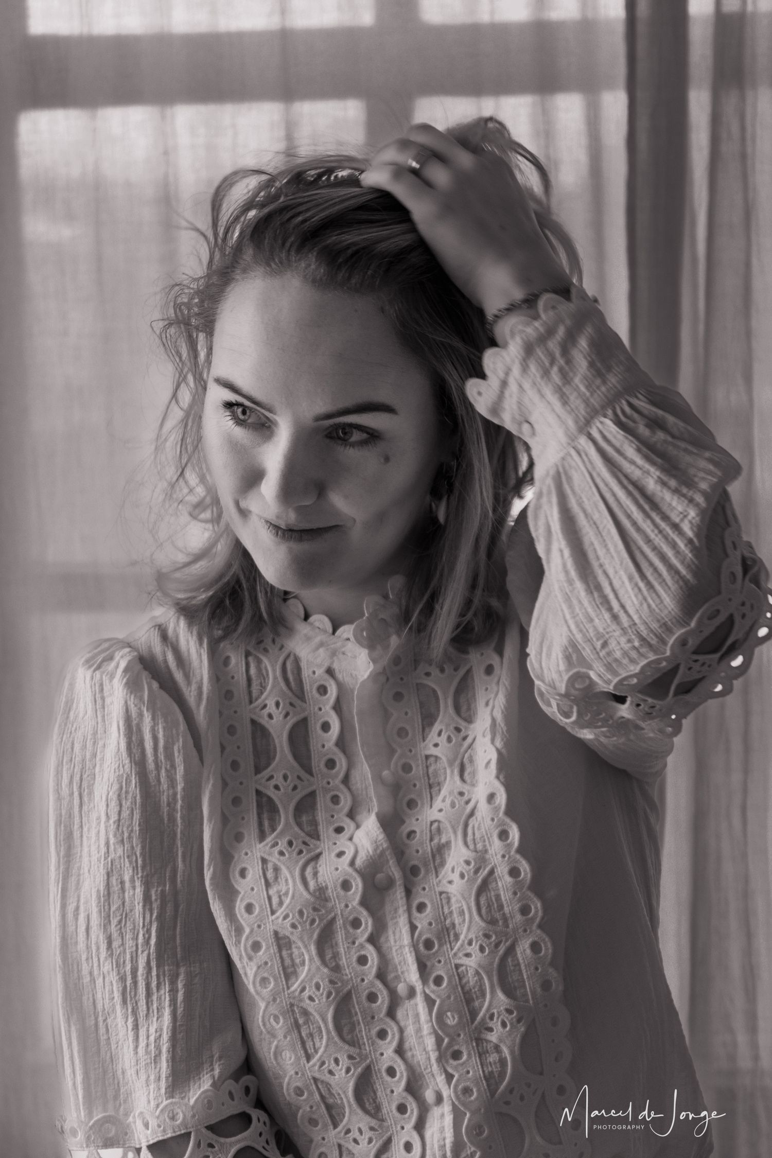 A series of black and white boudoir photos showing a person in lace clothing posing near sheer curtains.
