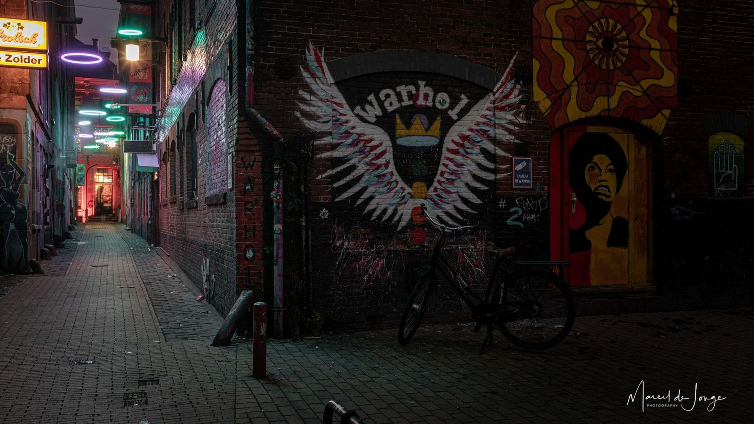 Neon-lit urban alleyway at night with graffiti artwork and illuminated storefronts creating a moody atmosphere.