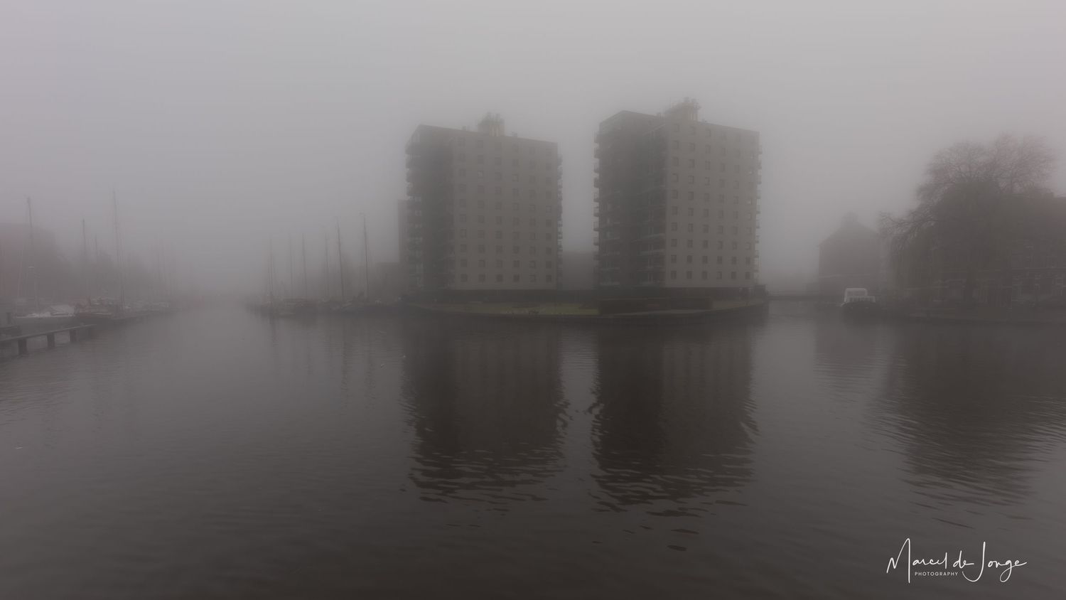 A misty panoramic cityscape shows tall buildings fading into dense fog along a waterfront.
