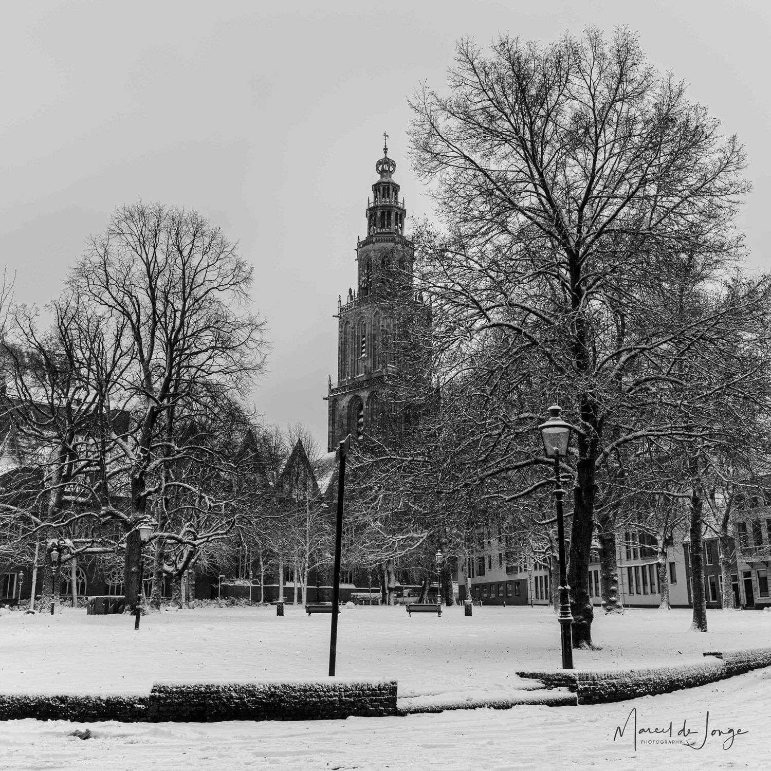 Snow-covered trees and church steeples create a serene winter panorama across a historic town square.