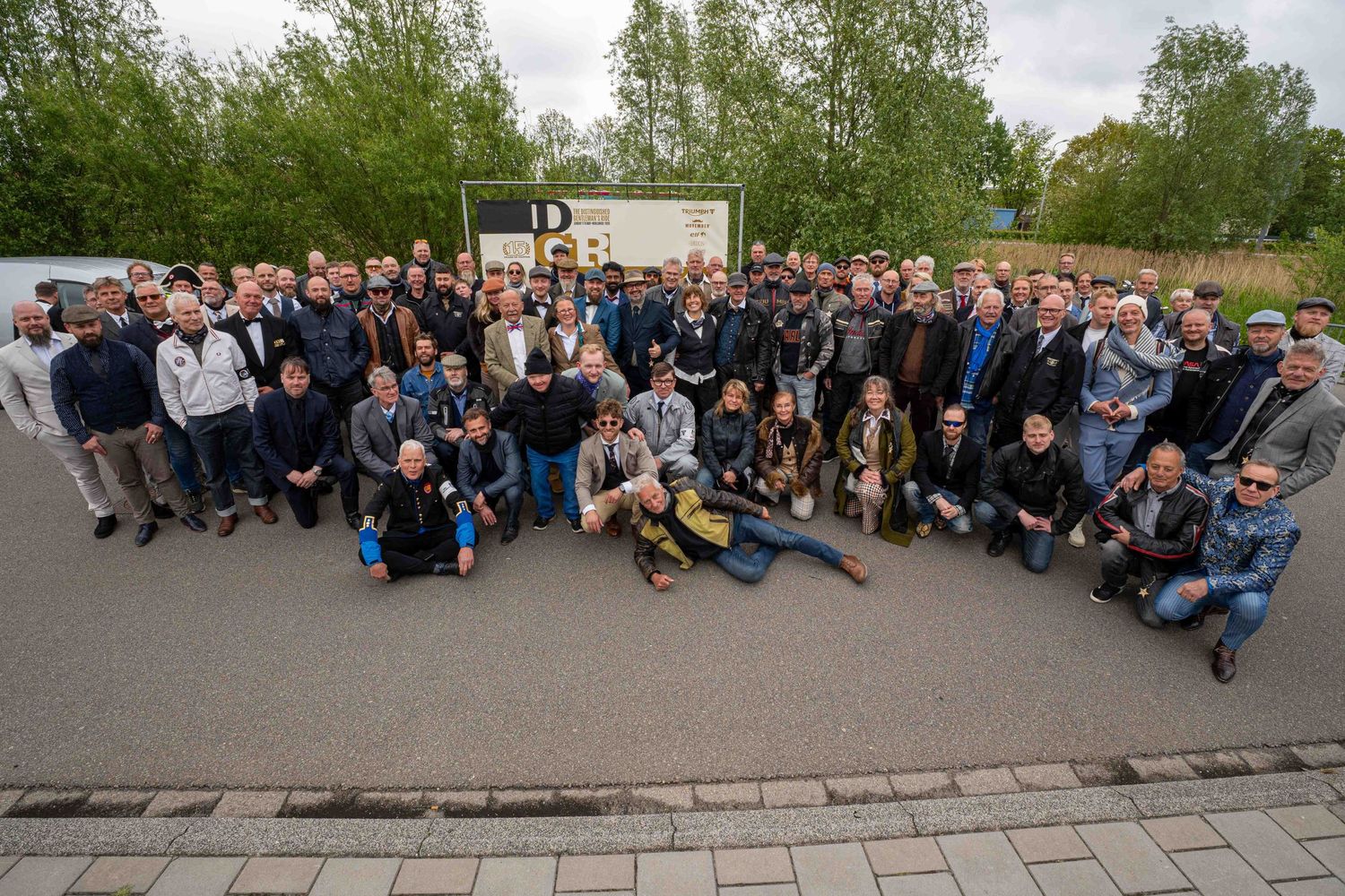Large group of professionals posing outdoors near a building sign for a corporate team photo event.