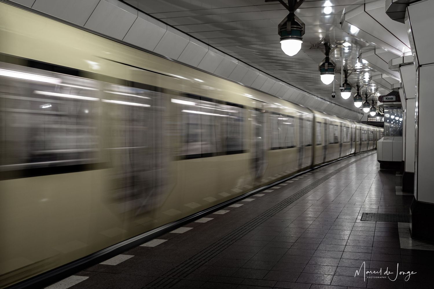 Dark subway tunnel with fluorescent lighting and tiled walls creates an eerie underground atmosphere.
