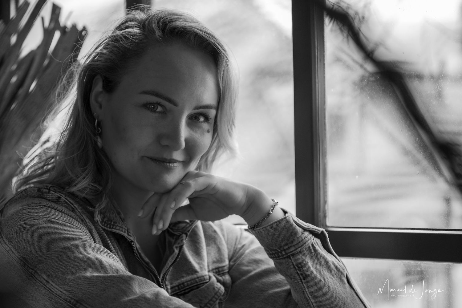 A black and white portrait of someone sitting by a window in natural light, resting their head on their hand.