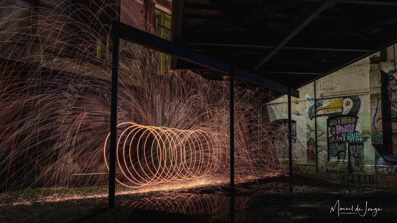 Long exposure photograph shows glowing steel wool spinning in circles creating light trails in an abandoned building at night.