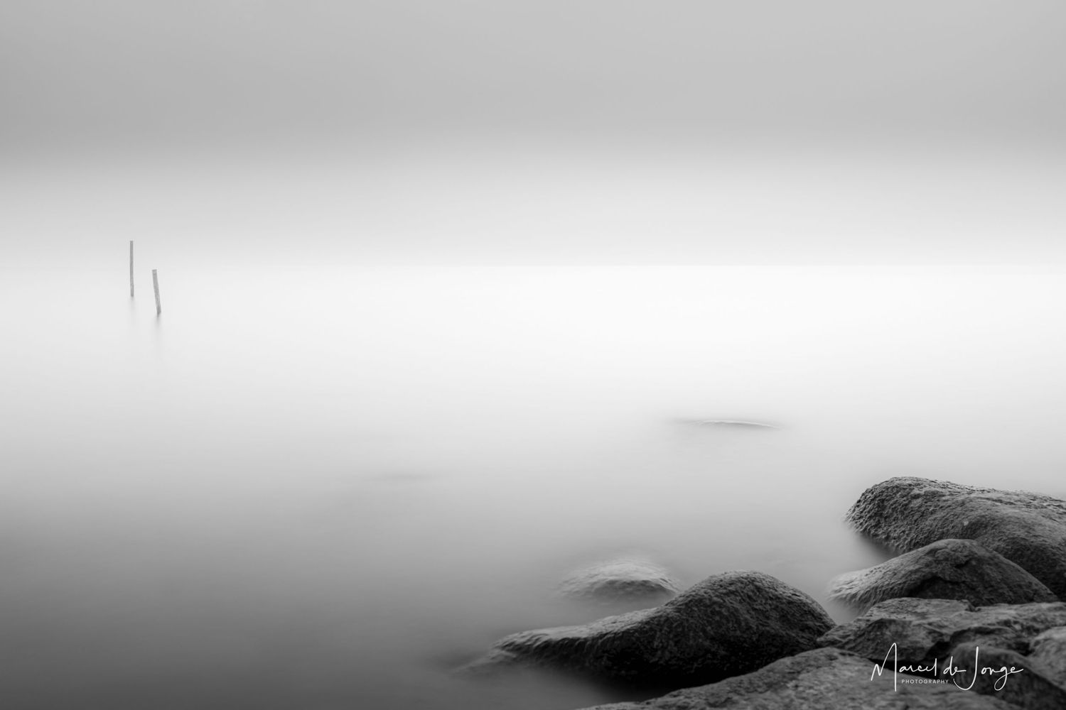 Dramatic black and white landscape of foggy coastal cliffs with crashing waves against rocky shoreline.