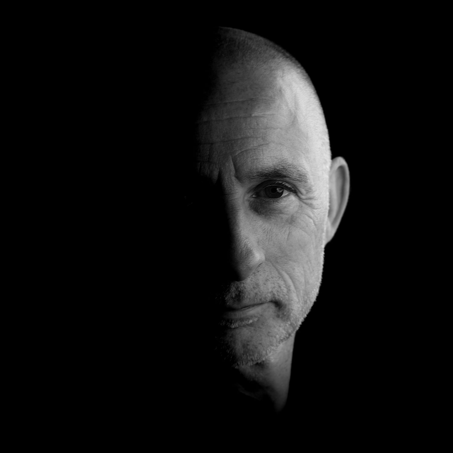 A dramatic black and white portrait emerging from shadow.