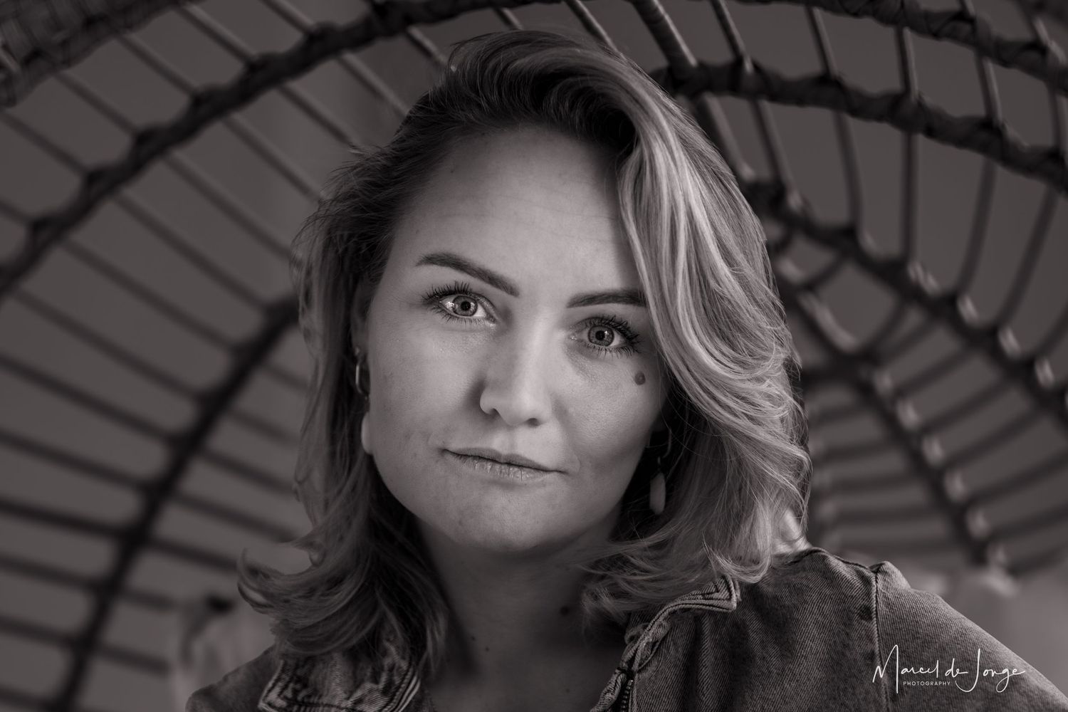Black and white portrait of a woman with wavy hair looking at camera through an arched architectural frame.