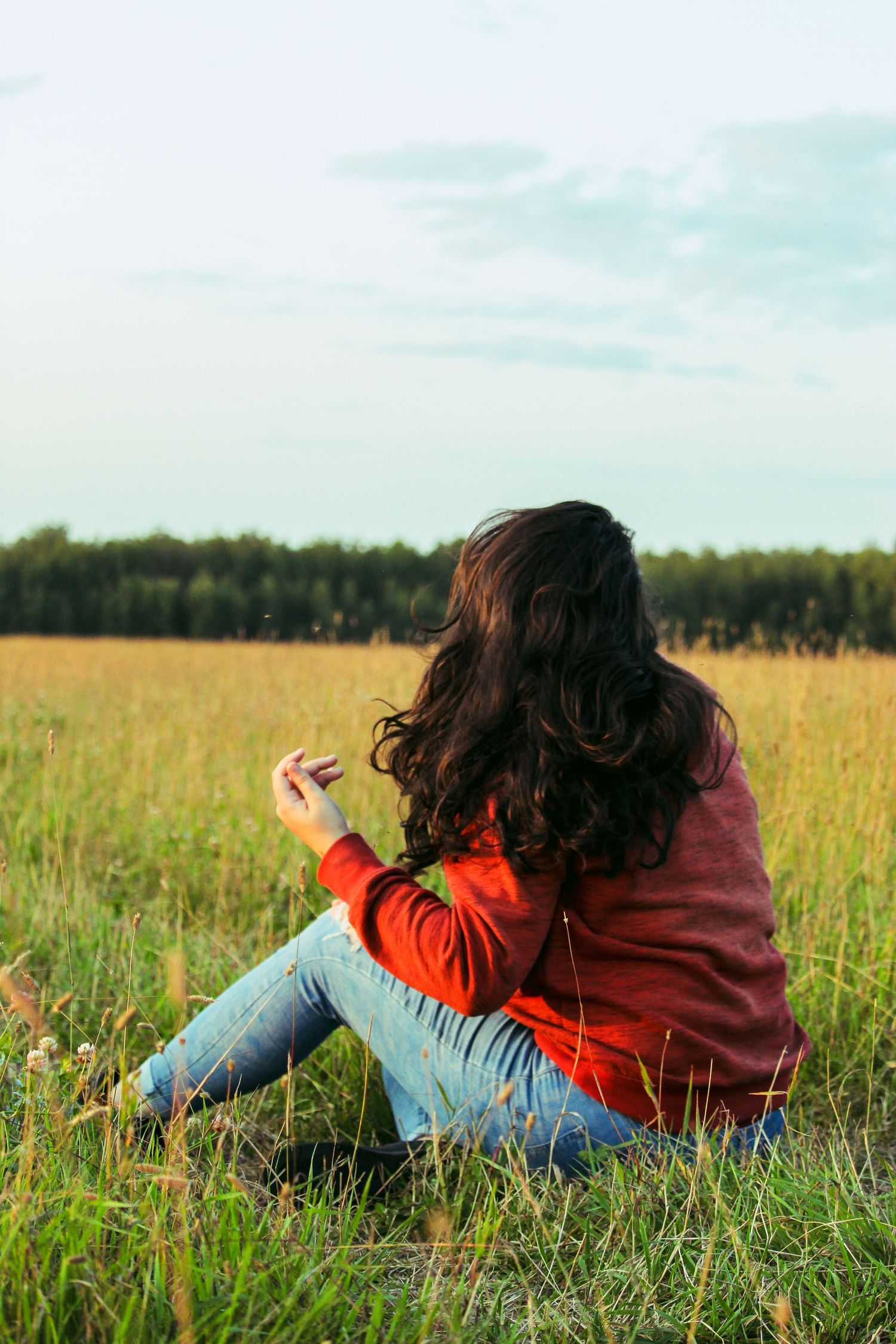 Woman sitting on ground in field with back to camera near Peace River, AB