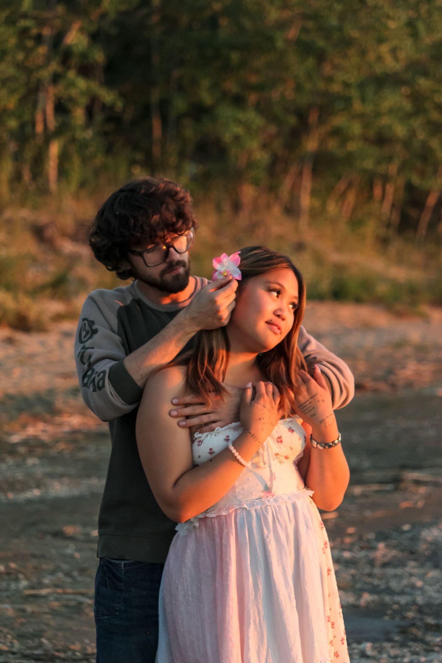 couple looking out at sunset on Lac Cardinal beach, man putting bow in woman's hair, holding each other
