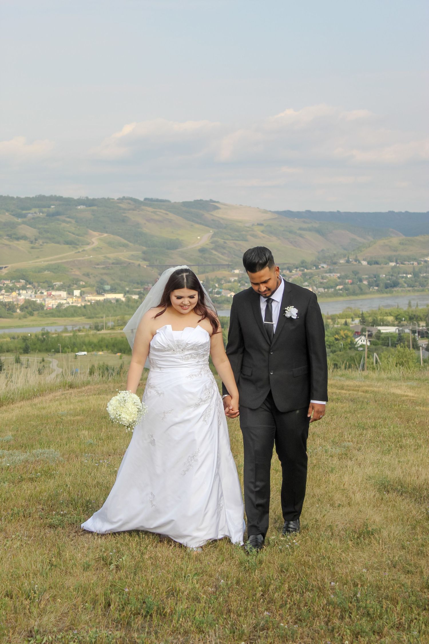 Couple walking in wedding attire overlooking the valley and town of Peace River