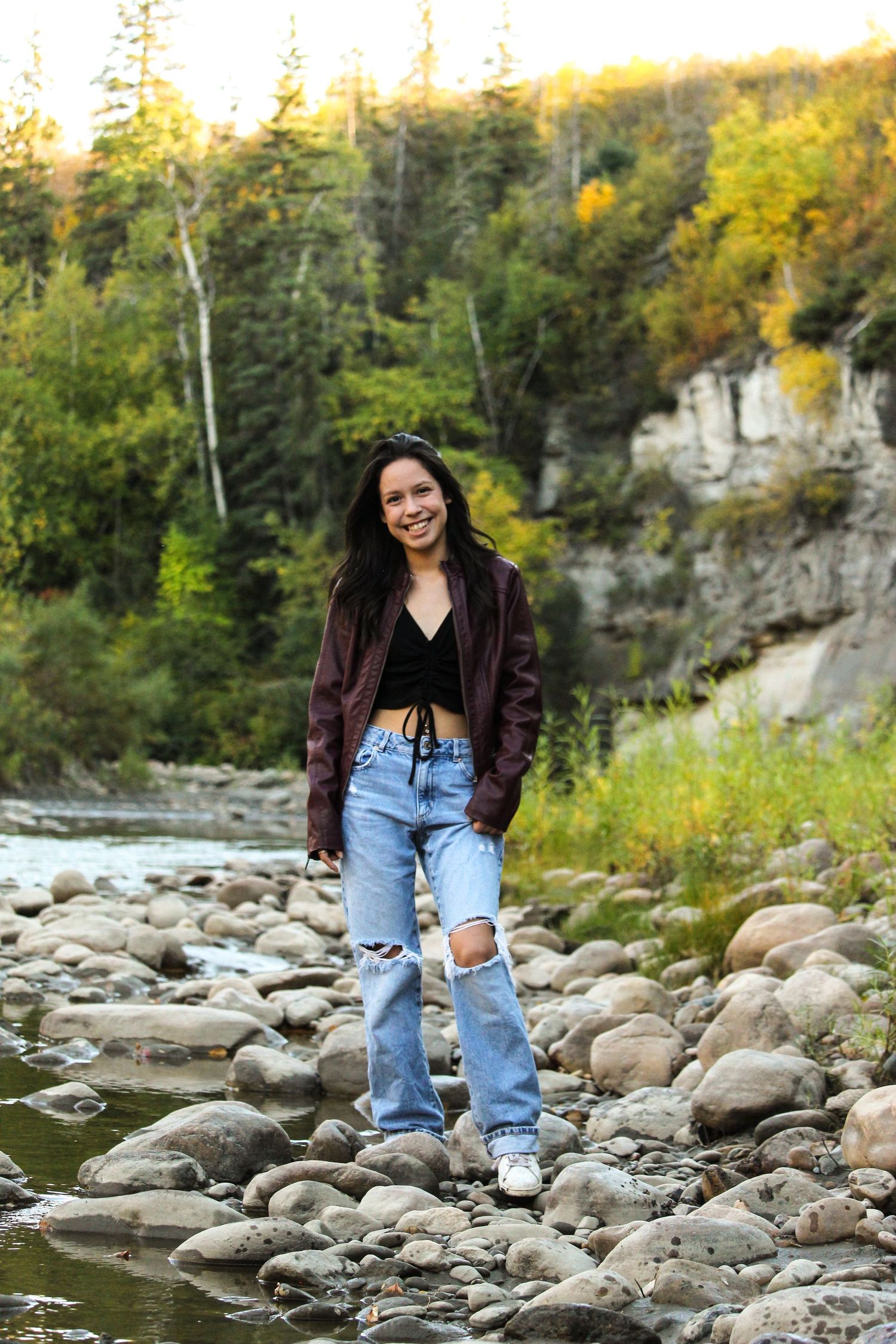 Girl standing on rocks with river and cliff behind her, fall theme in Peace River, AB