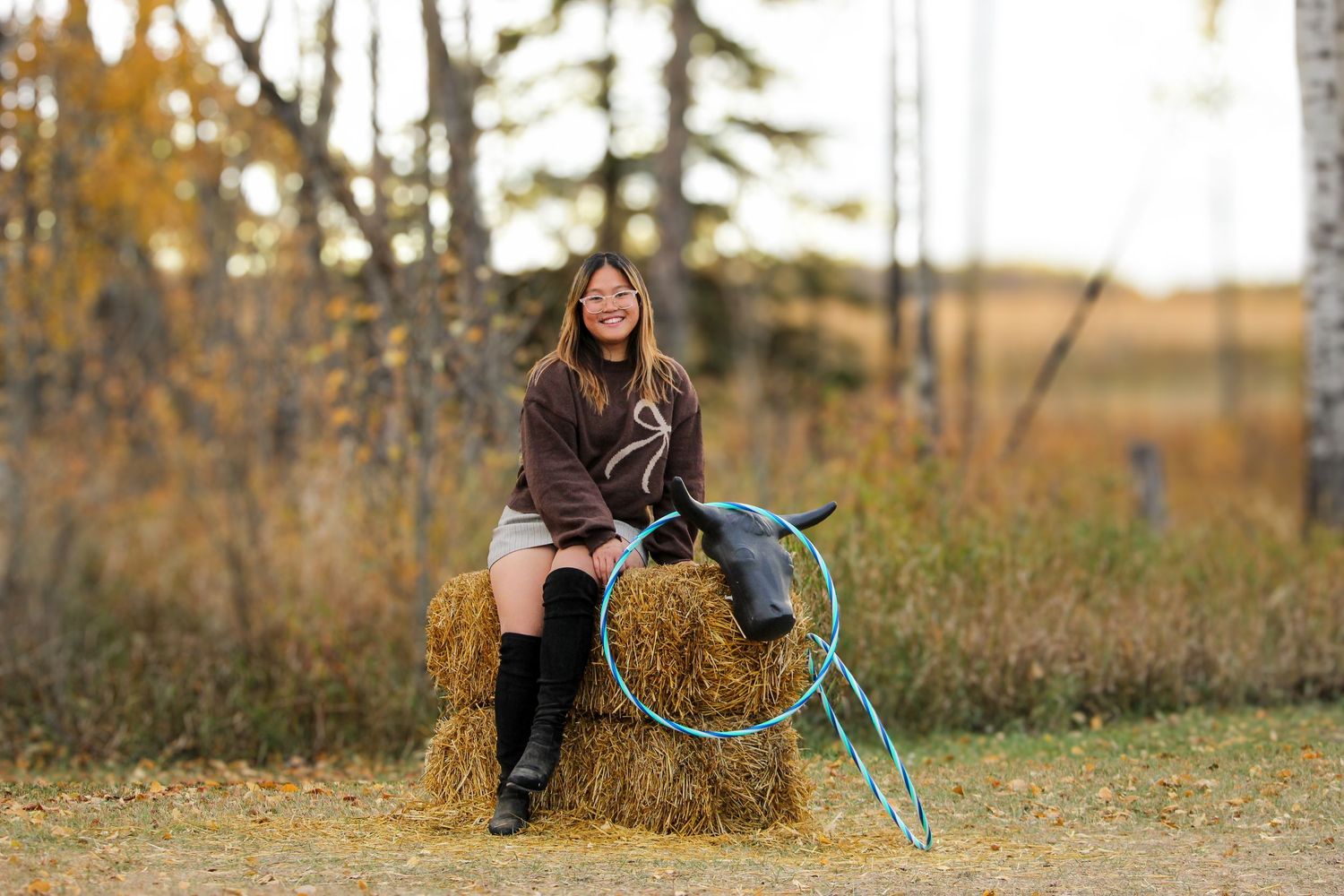 girl sitting on hay bales with fall background near Grimshaw, AB