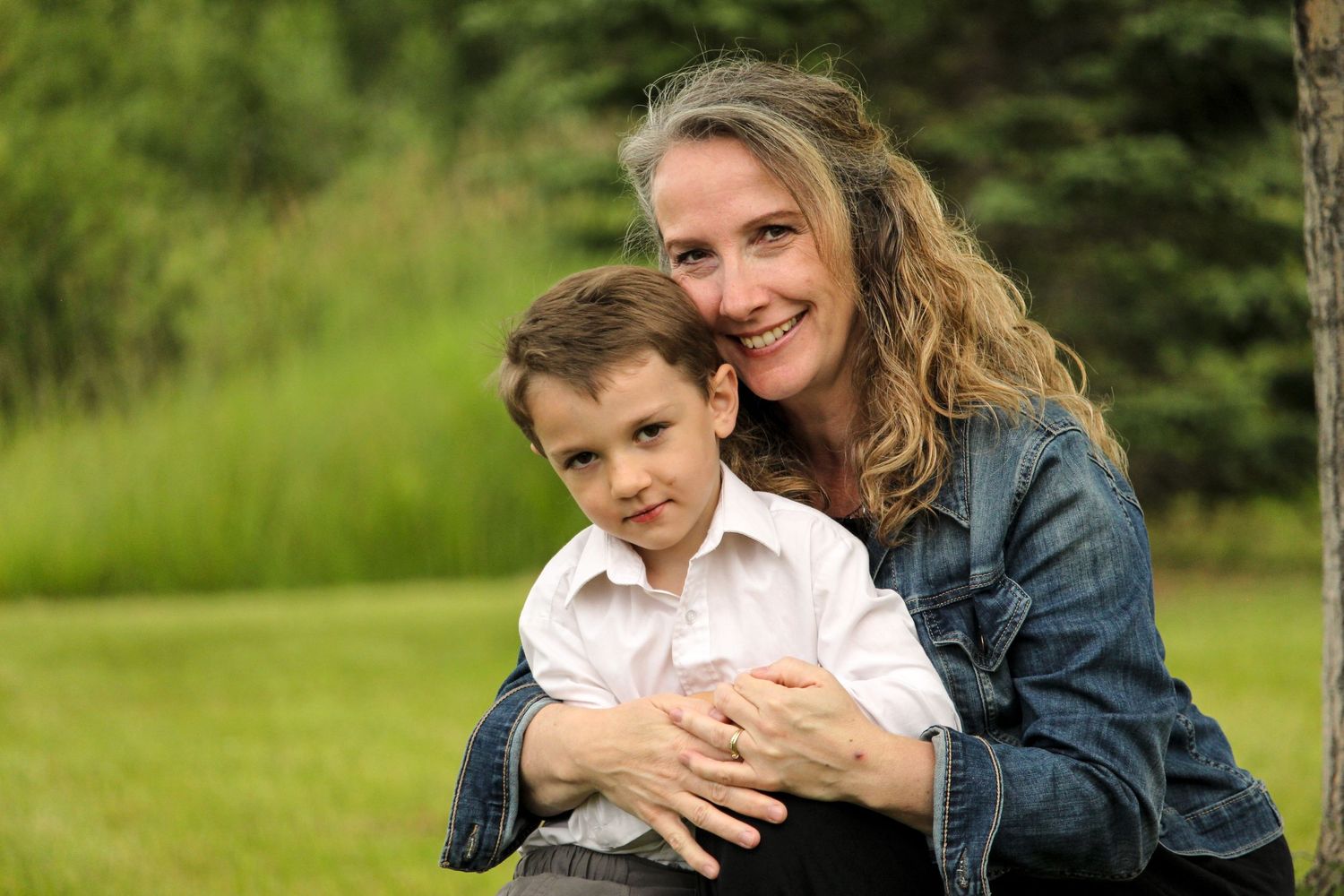 Mom and young boy hugging and sitting on grass in Rocky Mountain House, AB