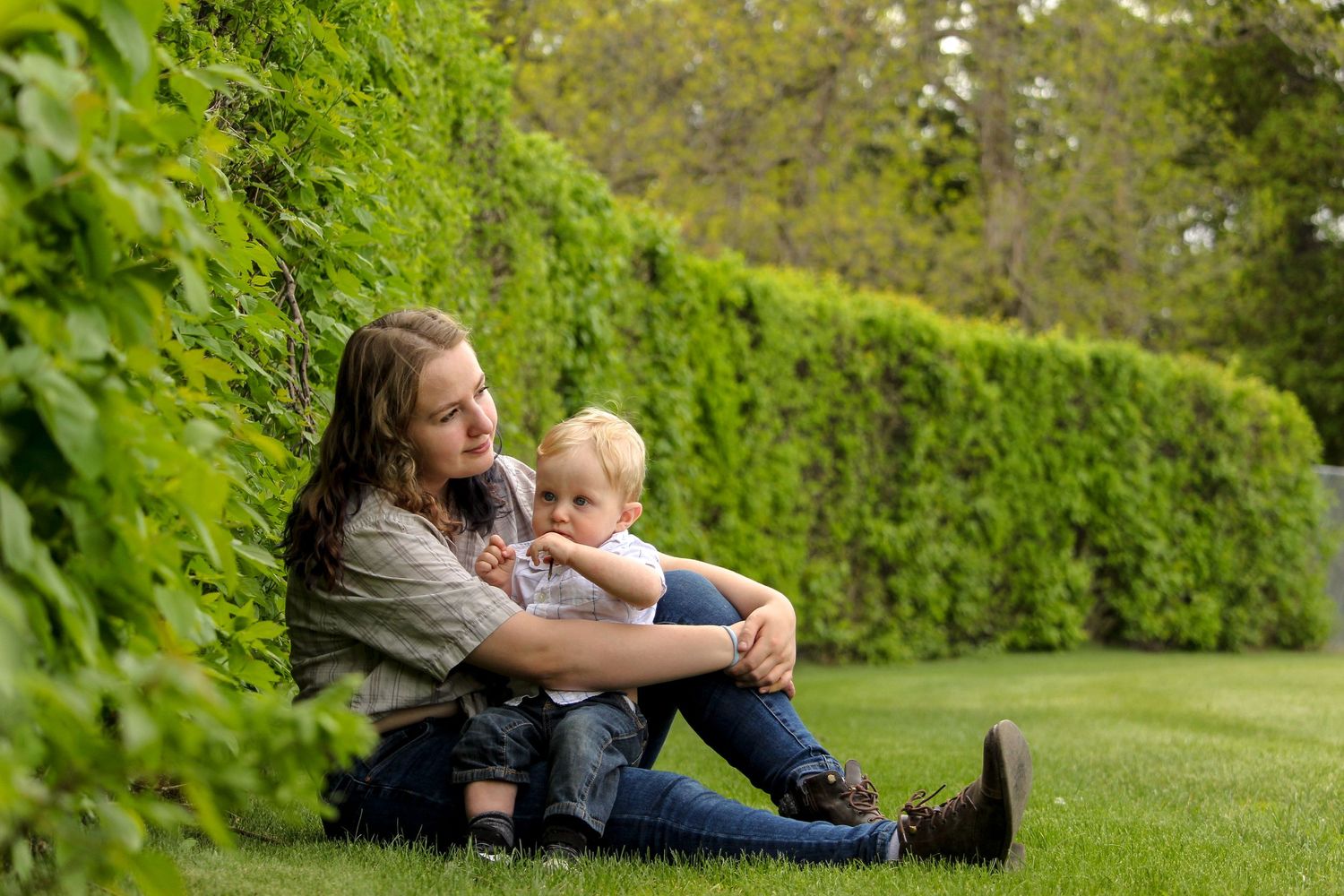 mom and baby boy sitting beside hedge, summer in Red Deer, AB