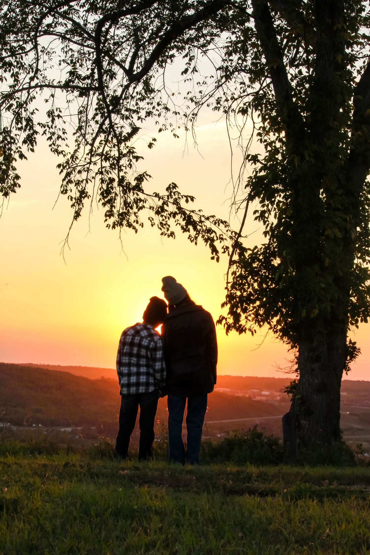 Brother and sister sillouette leaning on each other under tree overlooking Peace River, AB
