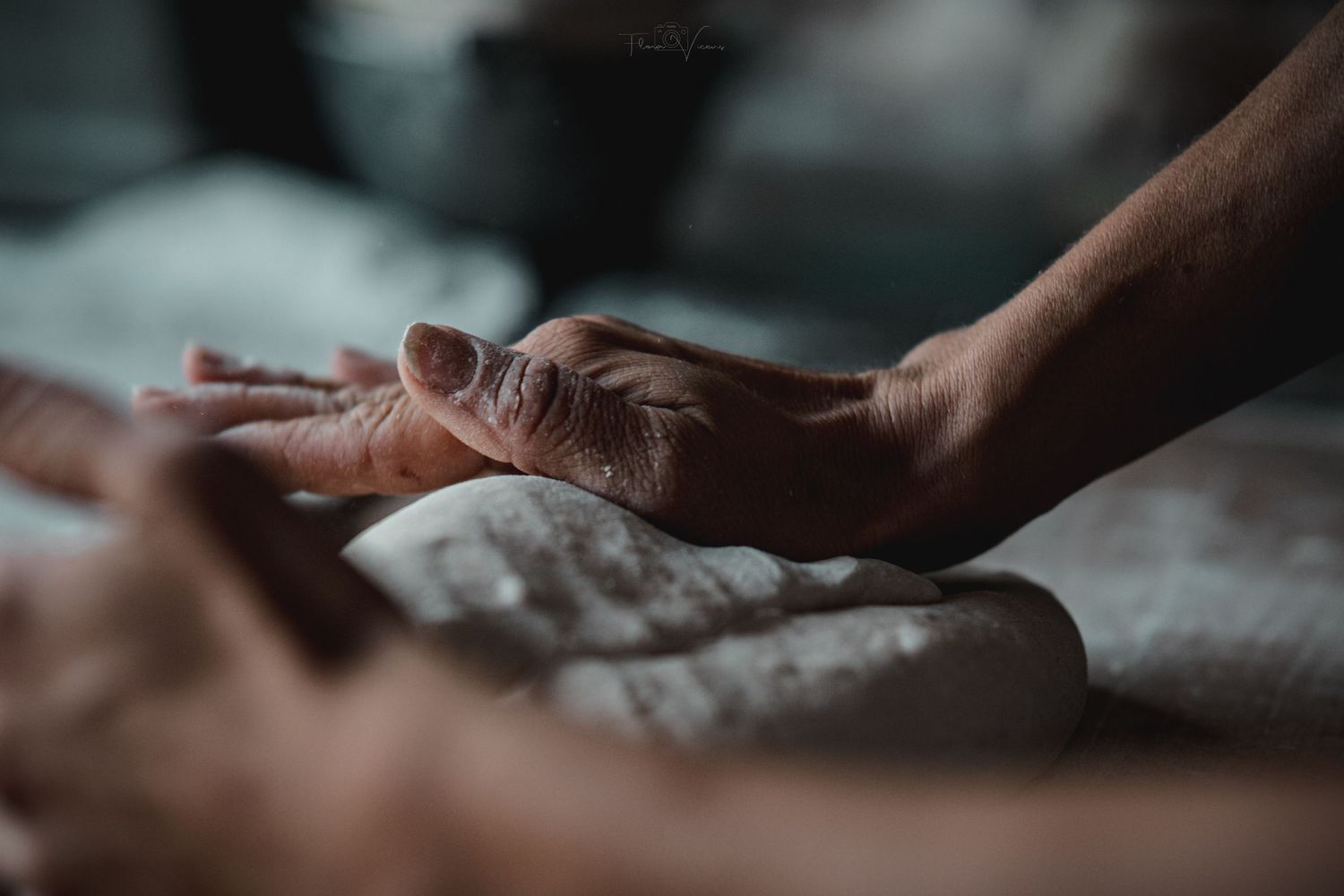 Hands working with bread dough on a floured surface in moody lighting.