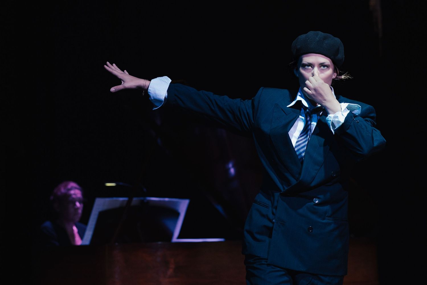 Performers in dark suits striking dramatic poses on dimly lit stage.