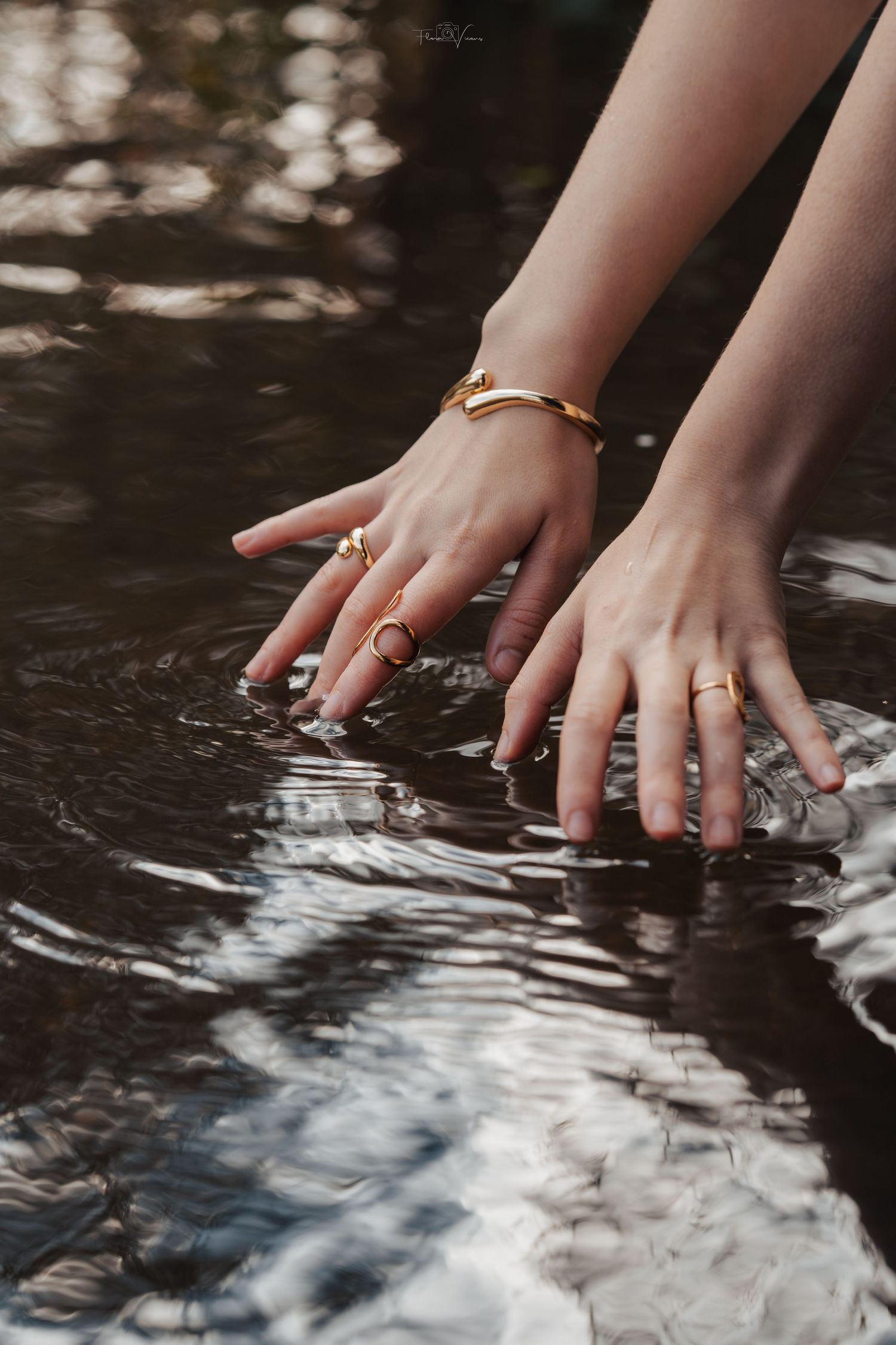 Hands with rings dipping into reflective water creating ripples.