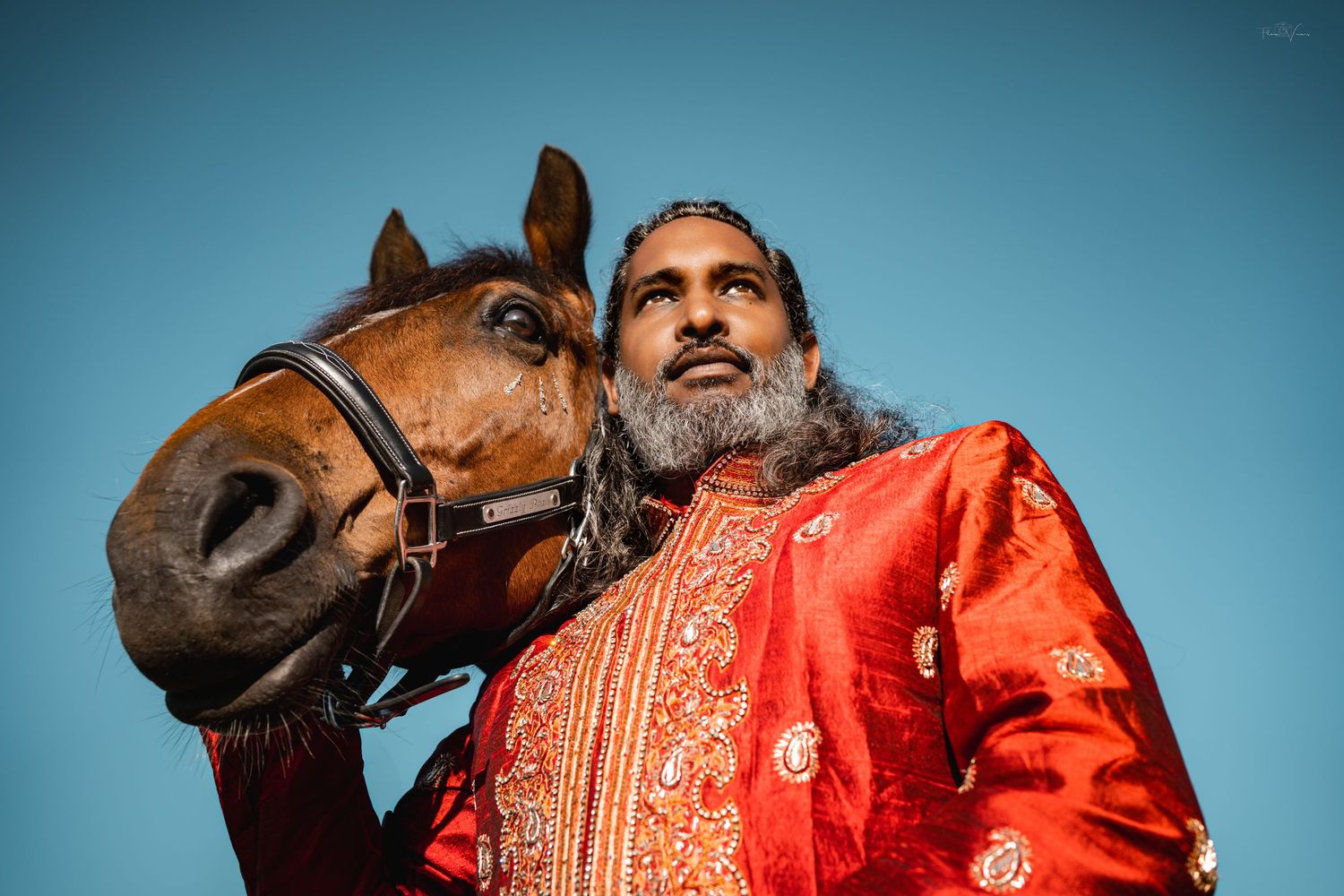 Horse and rider in traditional red dress against bright blue sky.