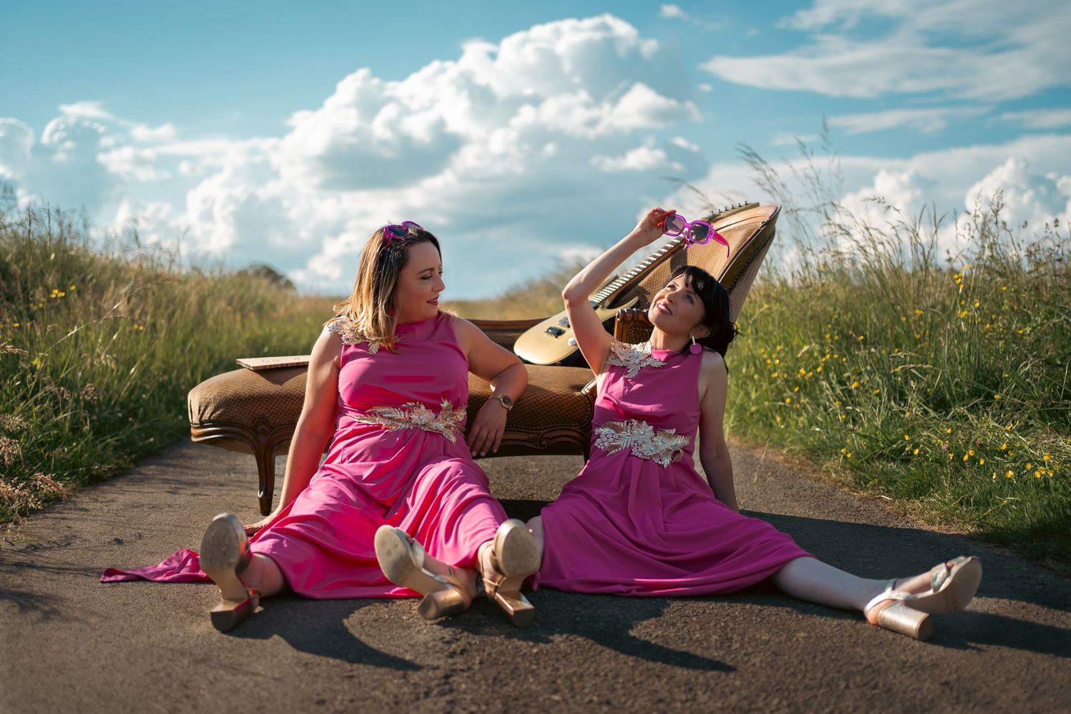 People relaxing in pink dresses on grassy hillside under summer sky.