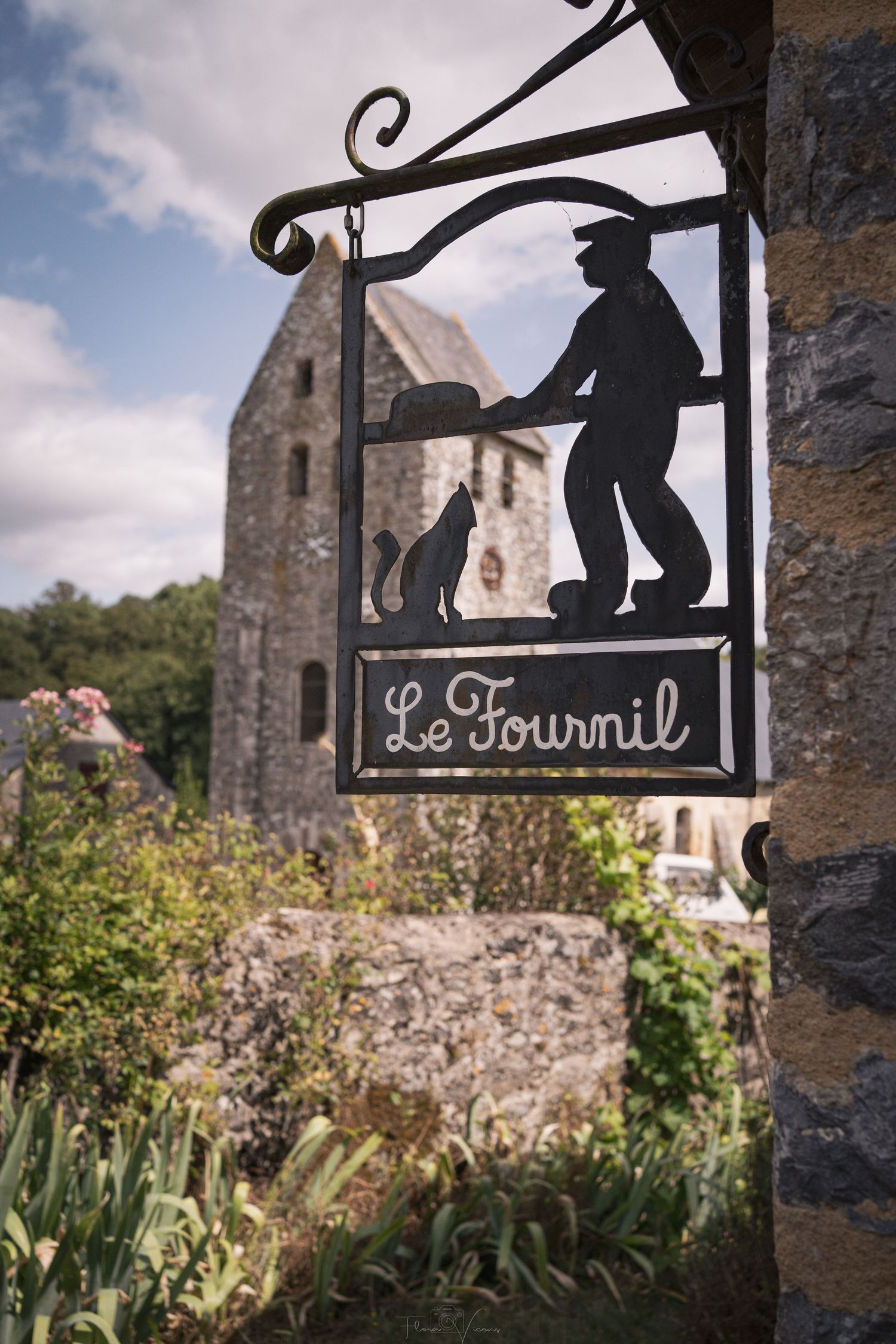Decorative wrought iron sign silhouette against stone wall and blue sky.