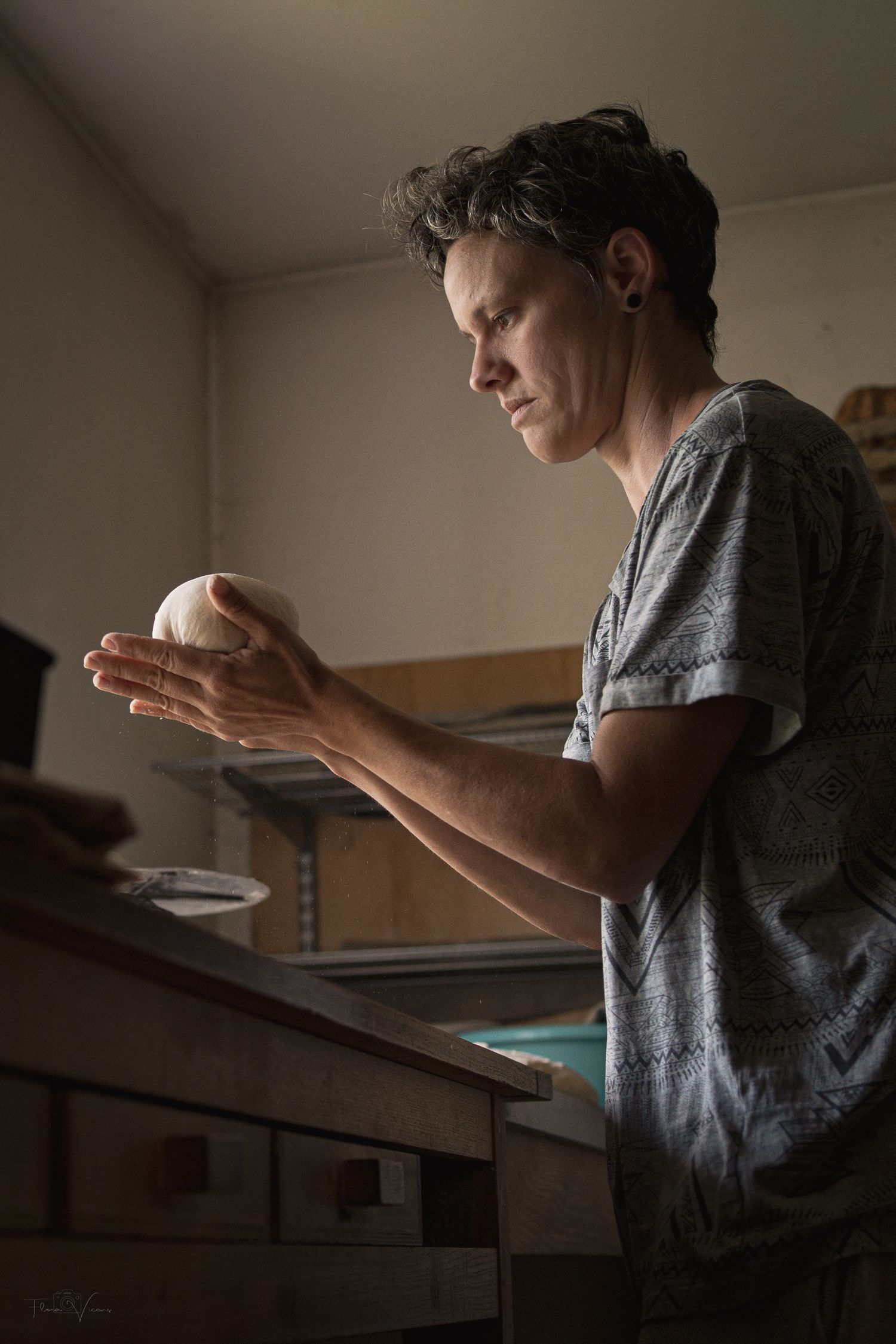 Baker working with dough in dramatic side lighting against a dark background.