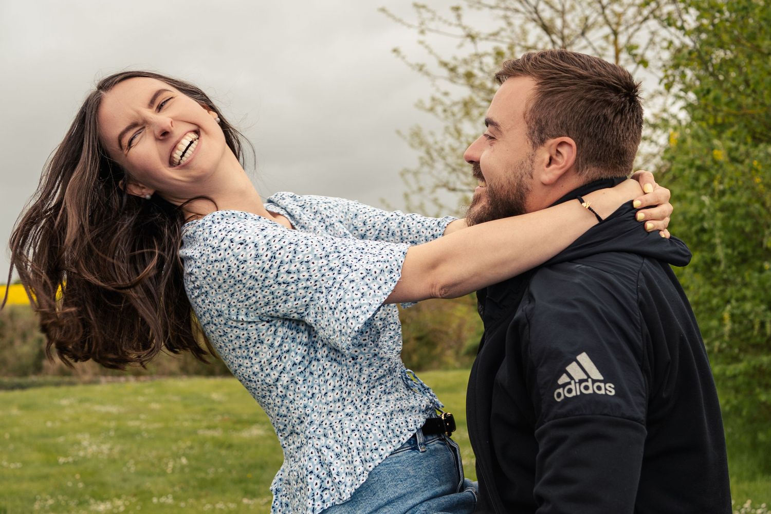 A couple shares a tender moment outdoors in casual clothing.