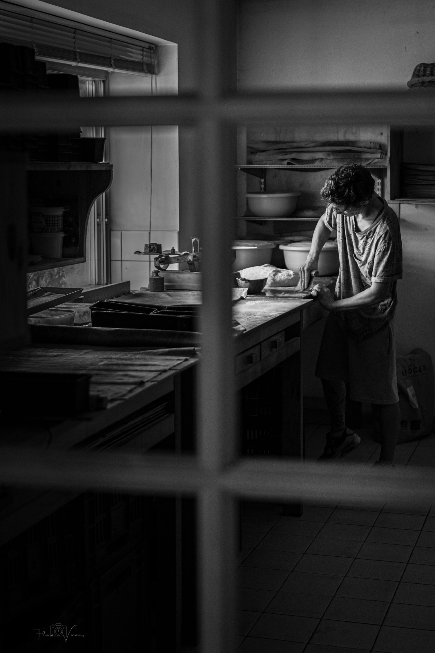Dark and moody view through window into a commercial bakery kitchen.