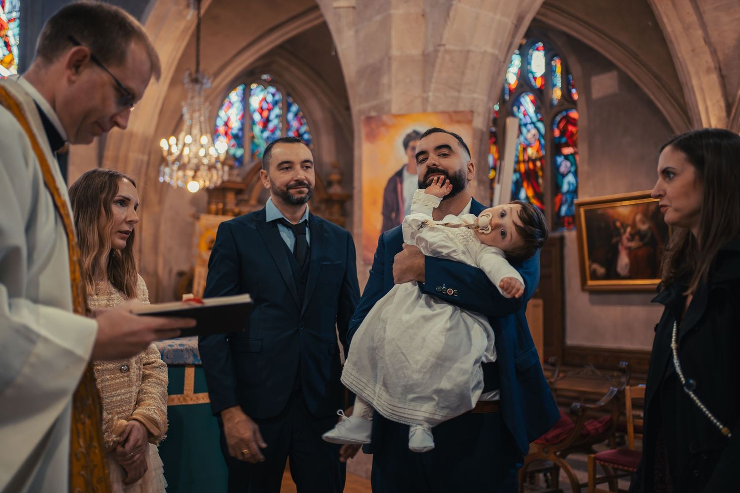 A traditional church ceremony with people gathered under ornate stone arches and chandeliers.