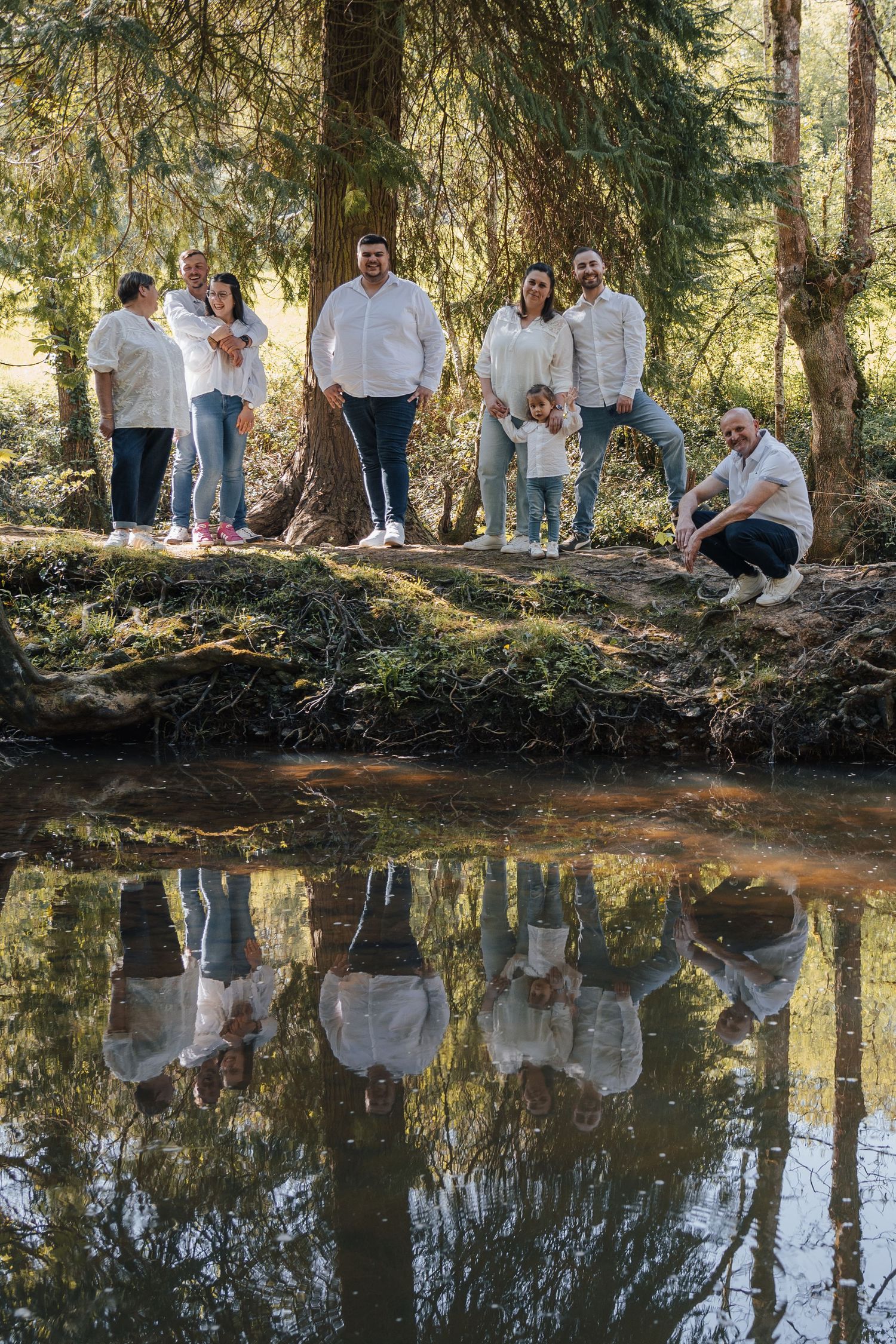 A group in white clothing poses along a reflective pond in a forest setting.