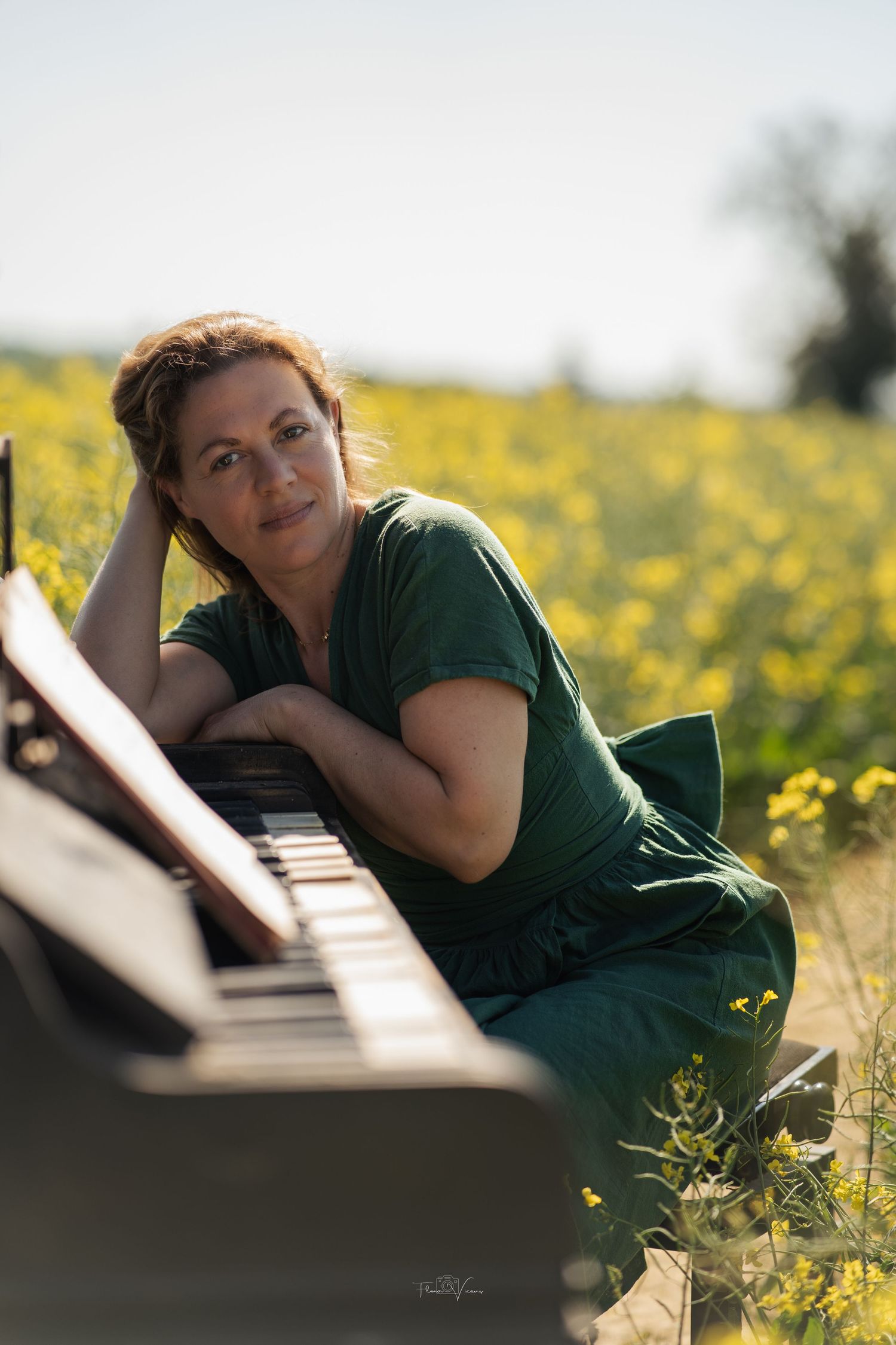 Person in green shirt resting near piano in field of yellow flowers.