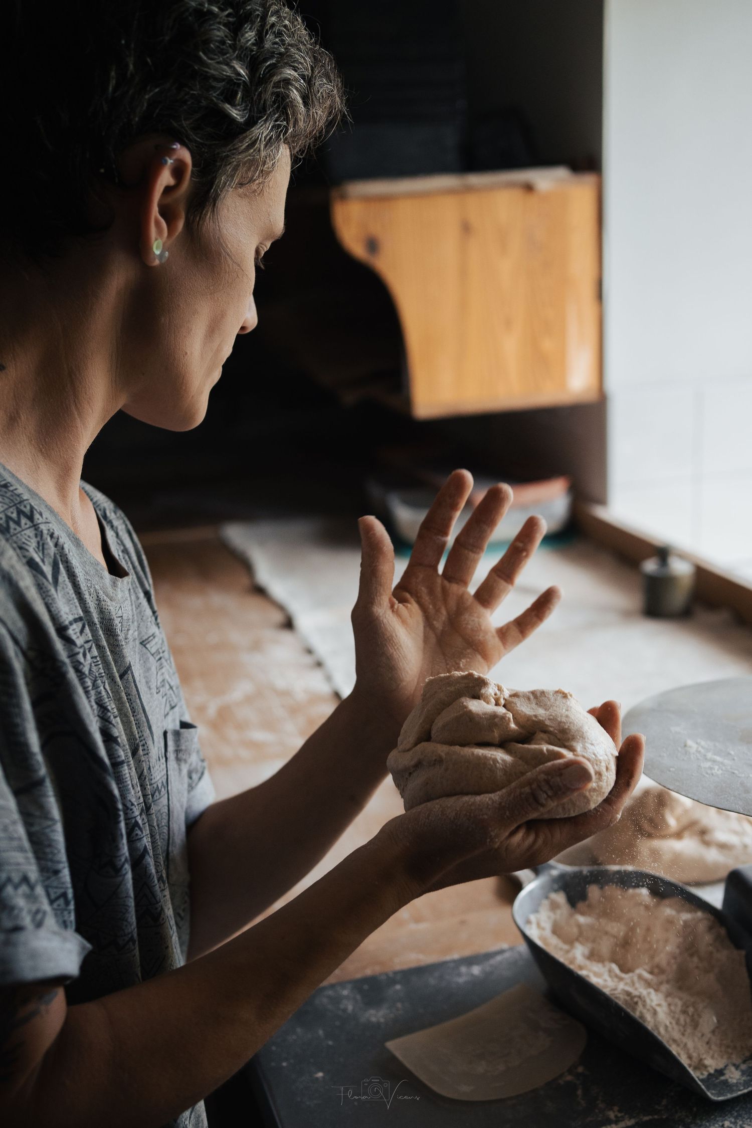 Hands shaping bread dough on a wooden table with natural light streaming in from the side.