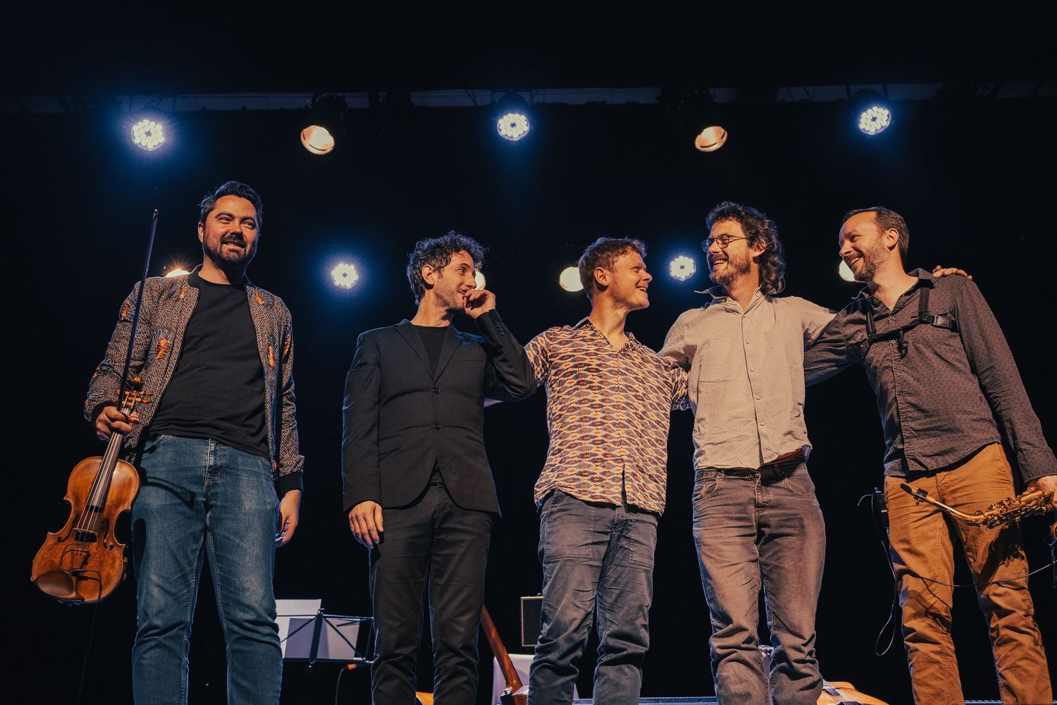 Group of performers taking a bow on stage under blue lighting.