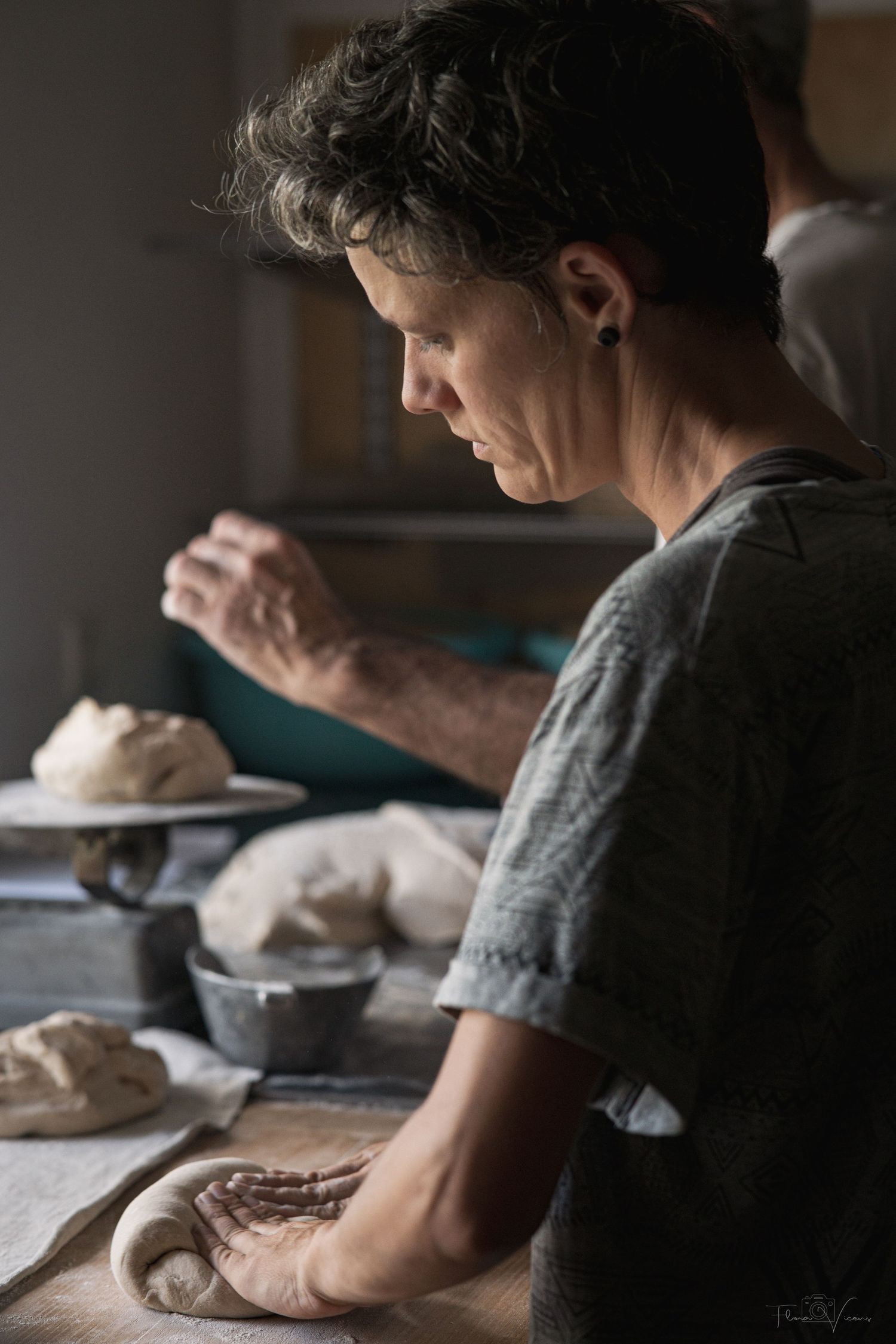 A person kneading bread dough on a floured surface in a rustic kitchen setting.