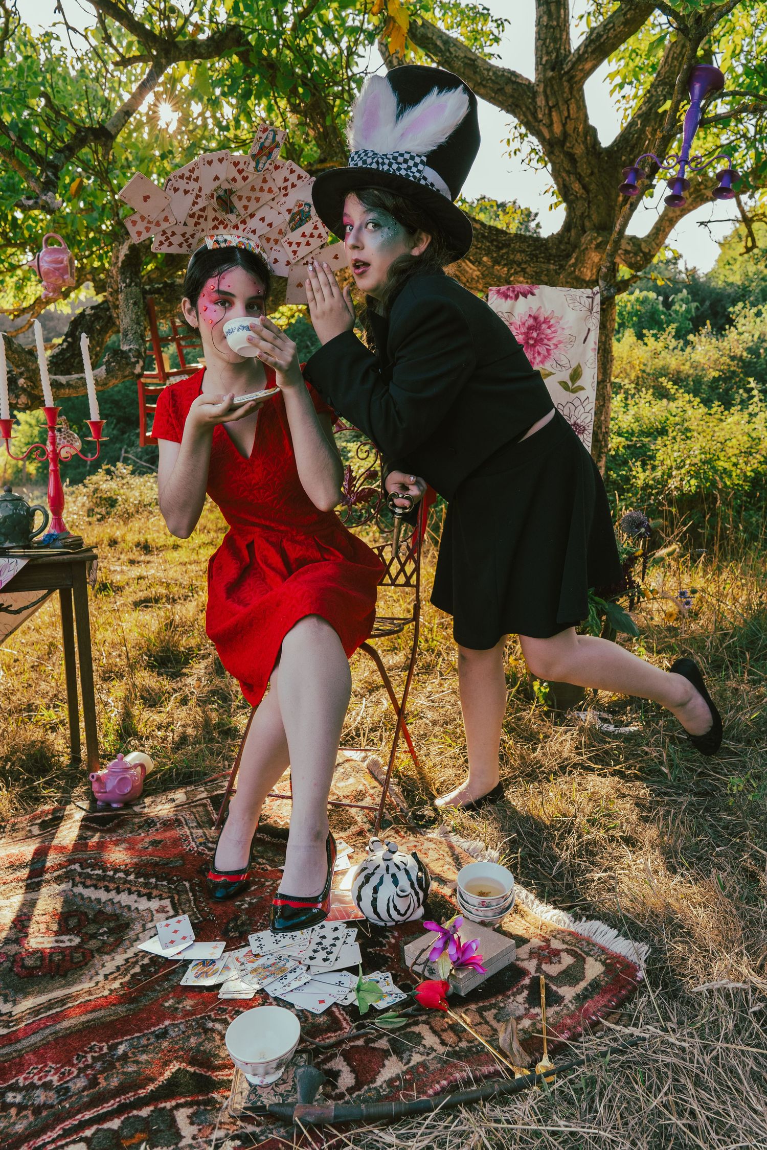 Two people having outdoor tea party with vintage decor under tree branches.