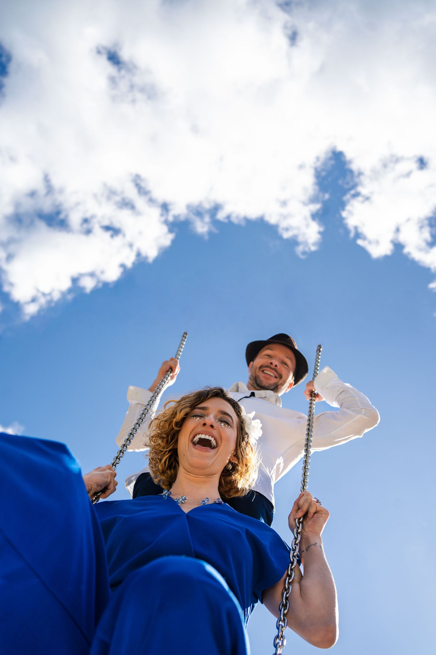 Person on a swing set against a bright blue sky with white clouds on a sunny day.