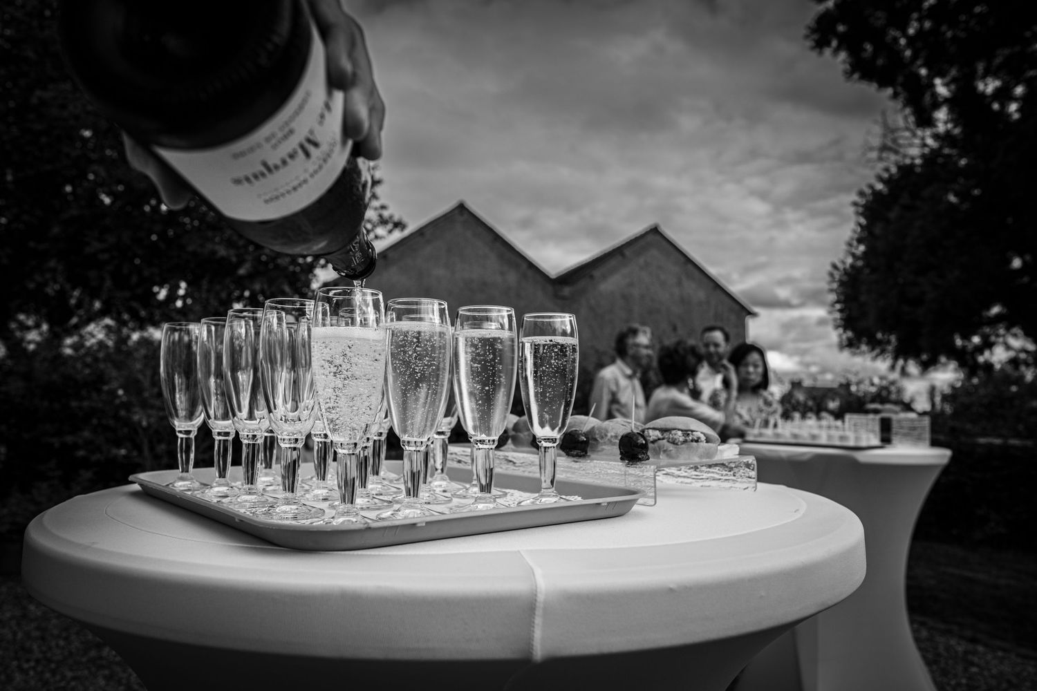 Row of champagne glasses arranged on white tables at an outdoor event.