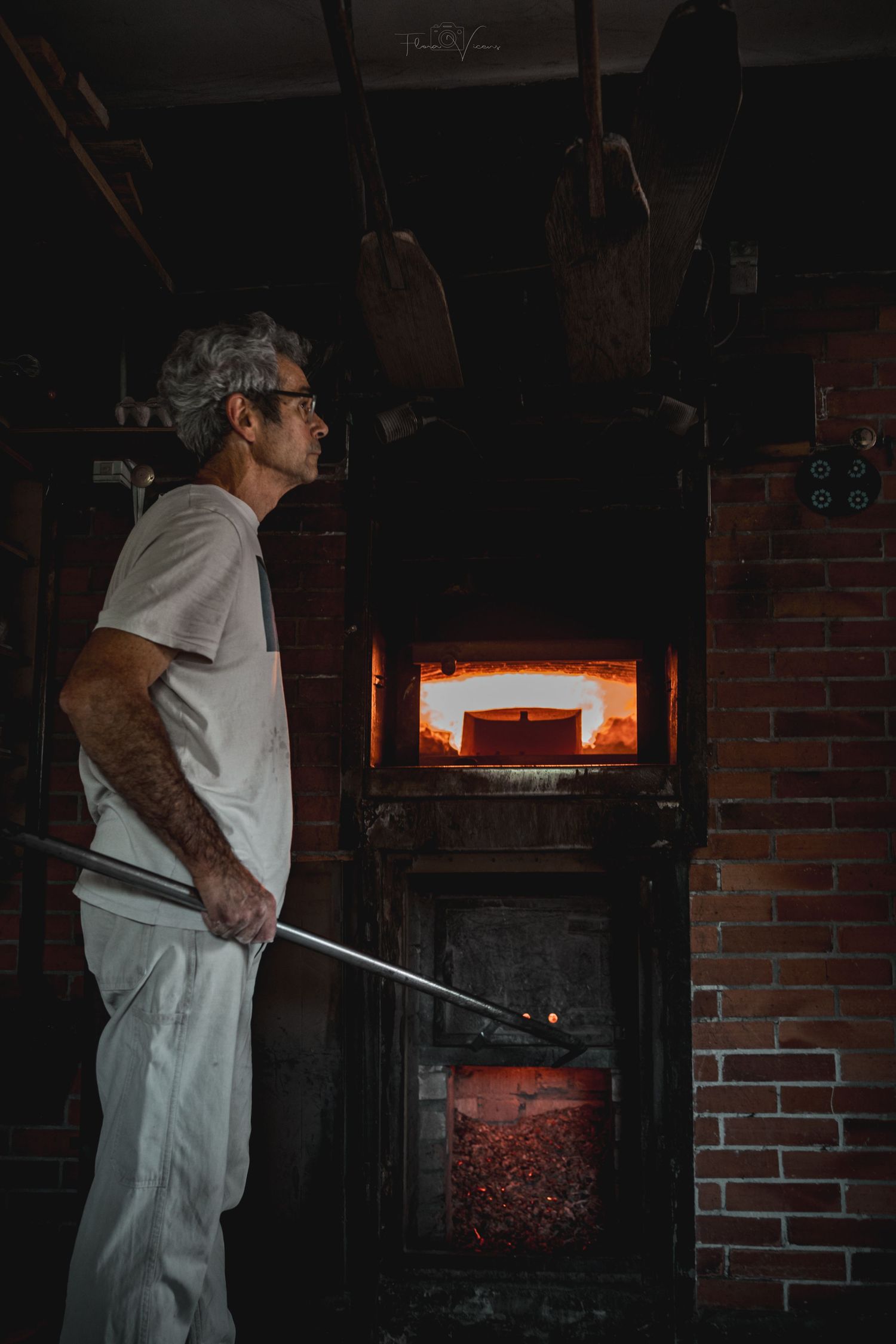 A baker works at a traditional brick pizza oven in white uniform.