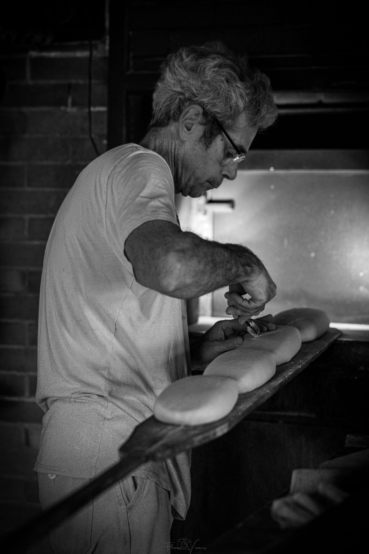 Baker working in dimly lit kitchen shown in dramatic black and white photography.