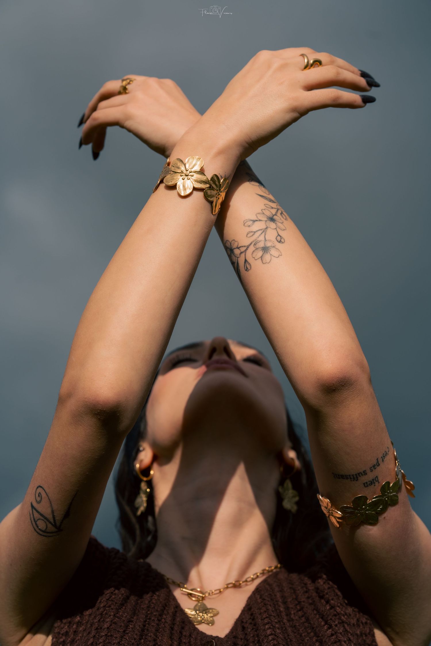 Artistic close-up of crossed arms showing delicate tattoos and jewelry against a dark background.
