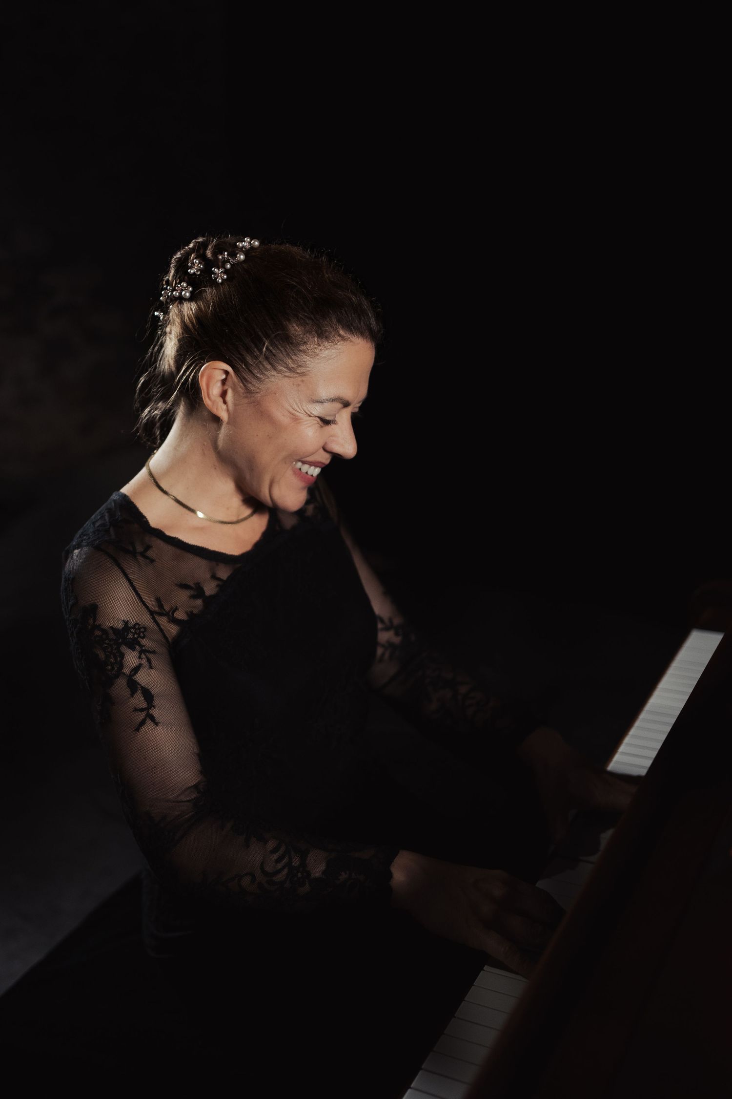 Pianist performing in dark setting wearing elegant lace attire.