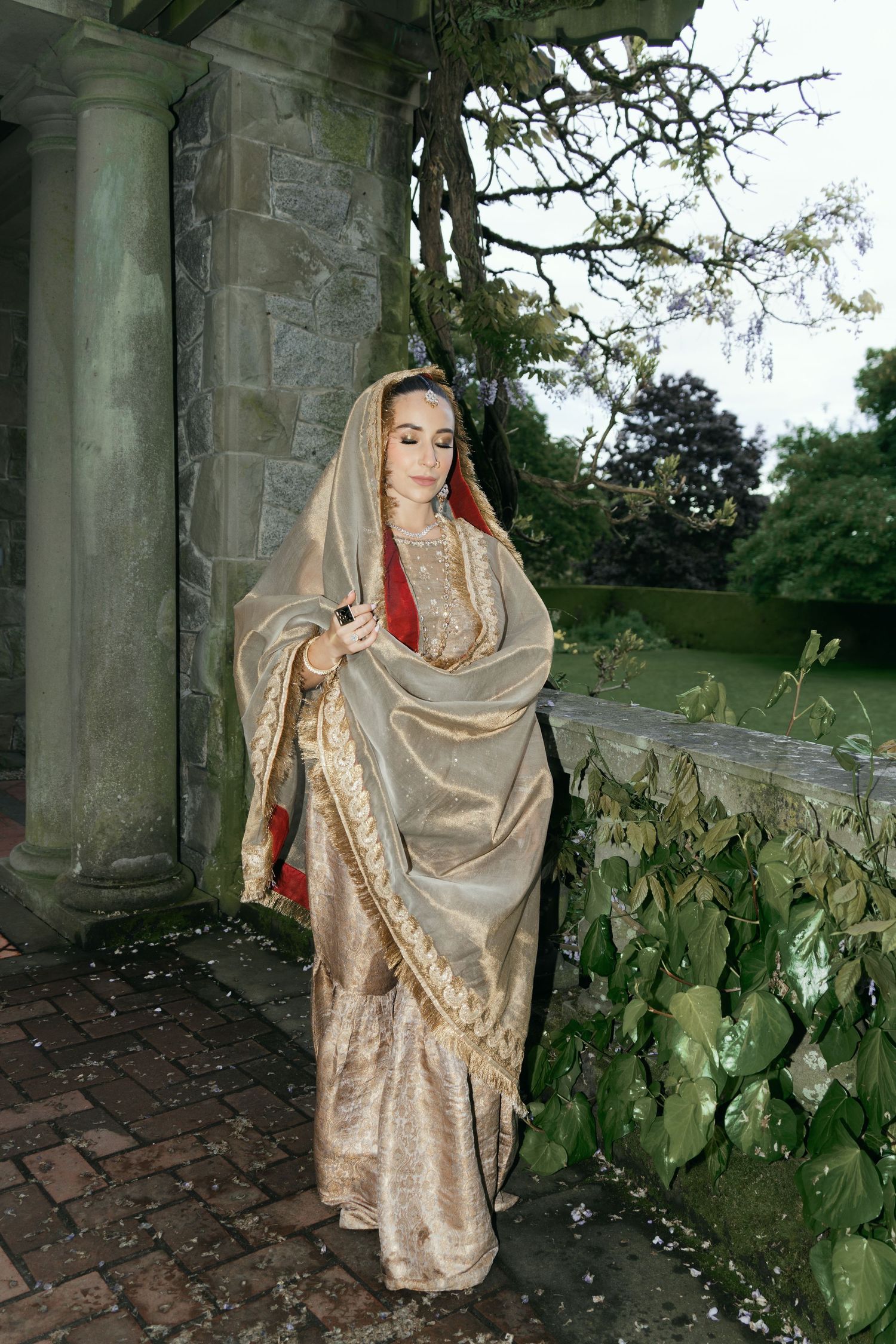 Figure in flowing golden dress poses dramatically against stone architecture.