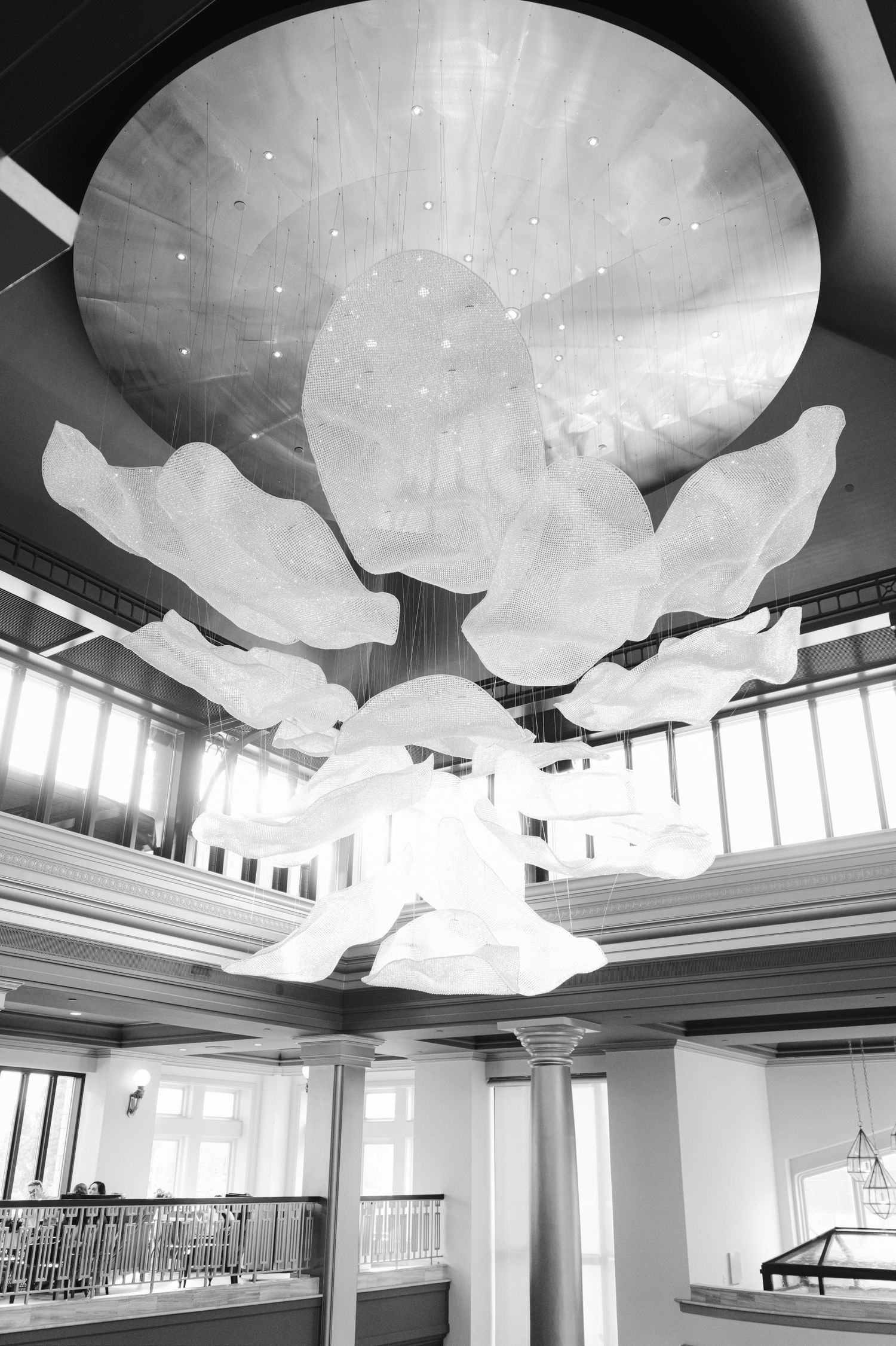 Black white photo of an elegant large floral chandelier hanging from a circular ceiling in a grand interior lobby at Fairmont Empress BC