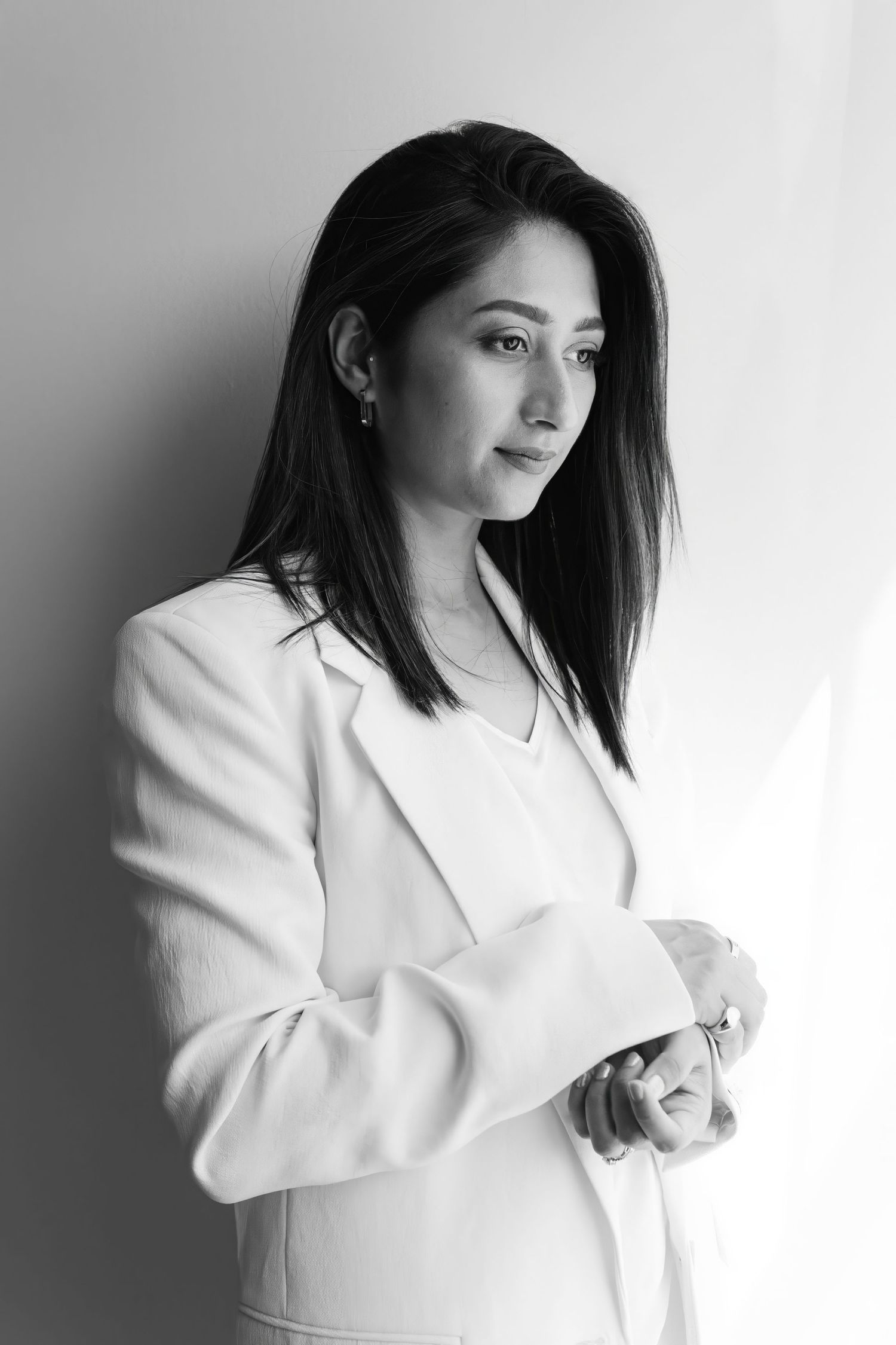 Black and white portrait against plain wall wearing white blazer.
