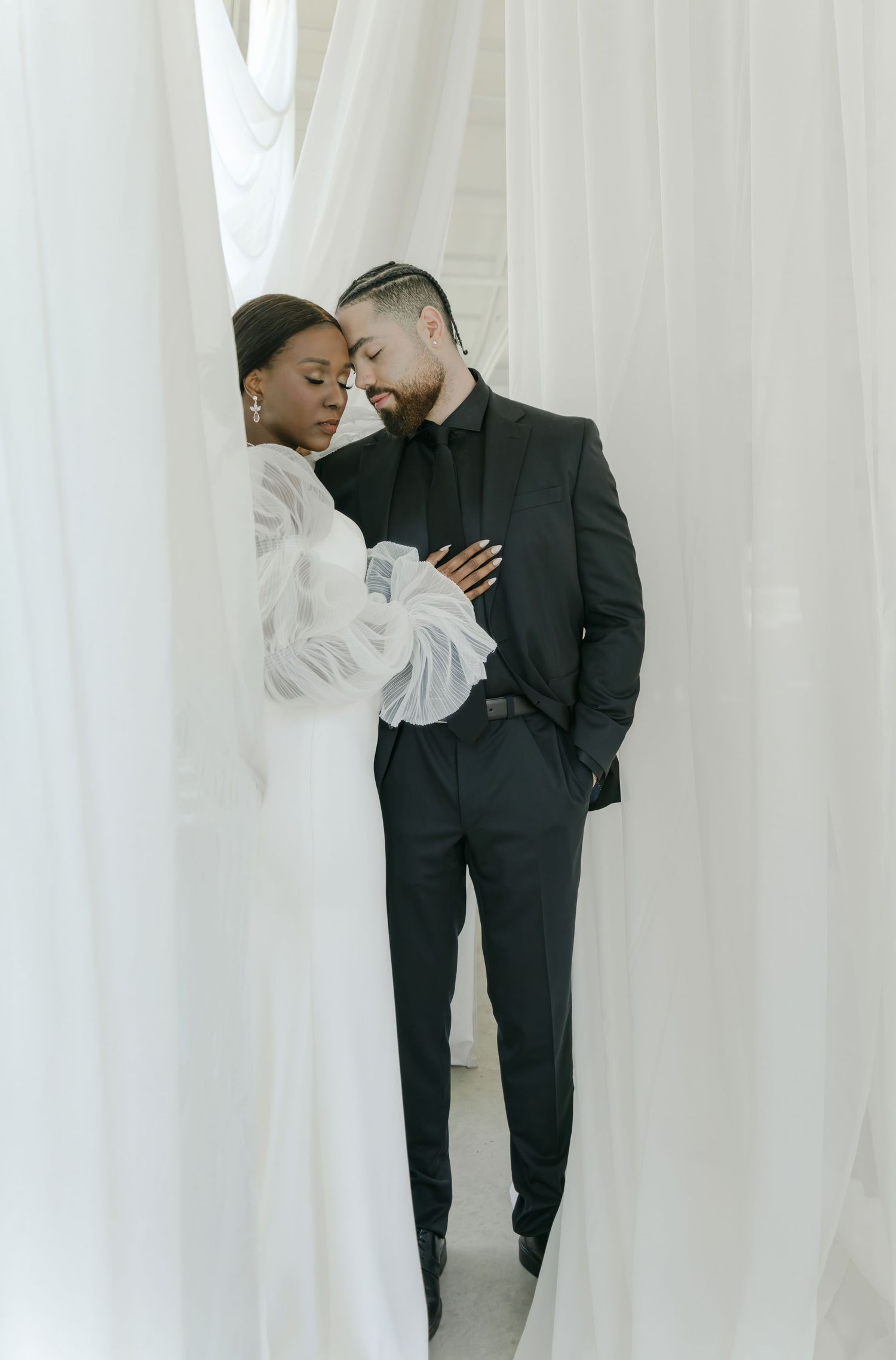 Romantic couple embracing in minimalist white studio setting with dramatic lighting.