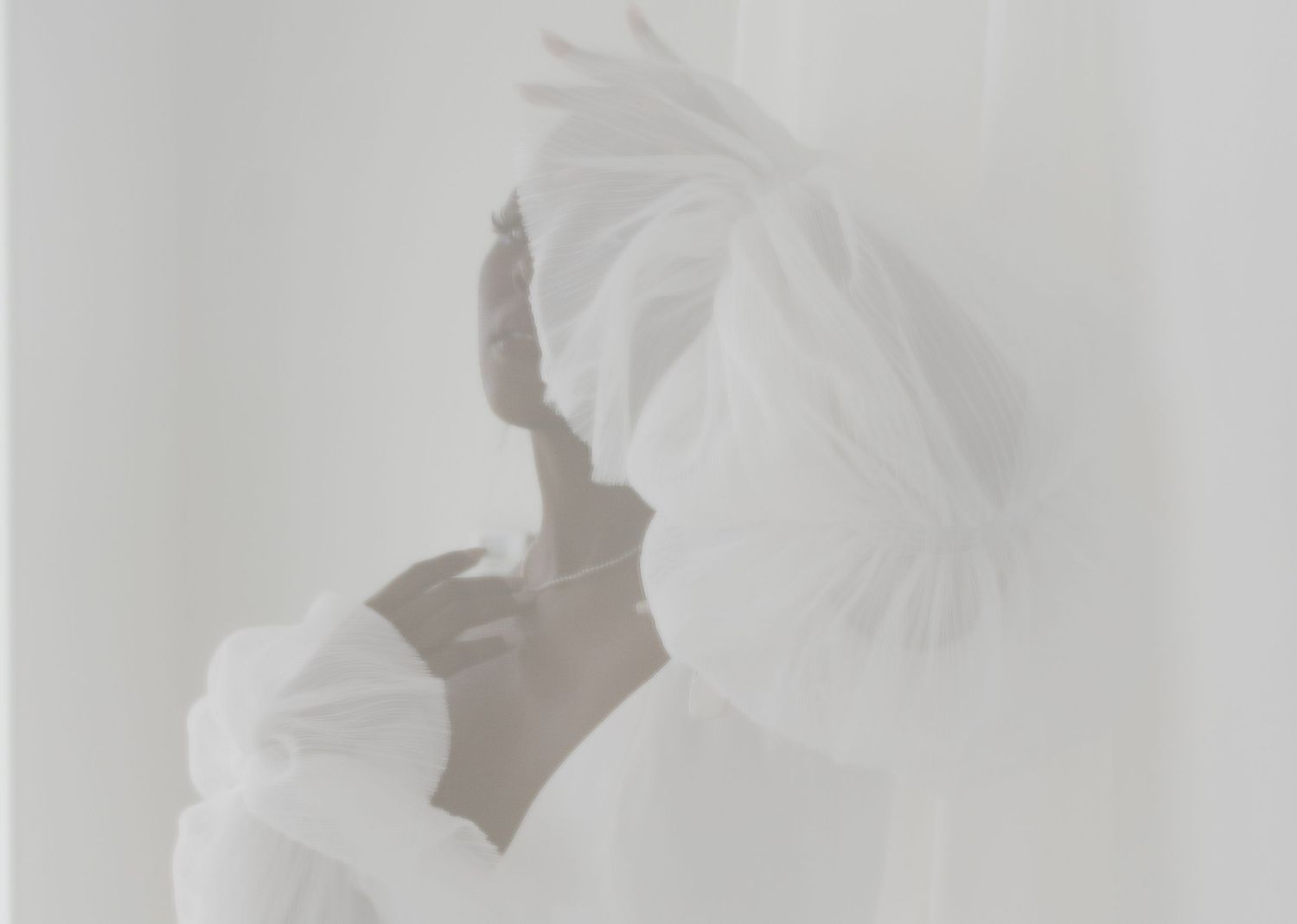 Ethereal woman in white holding a large feathered fan against a soft, dreamy white background.